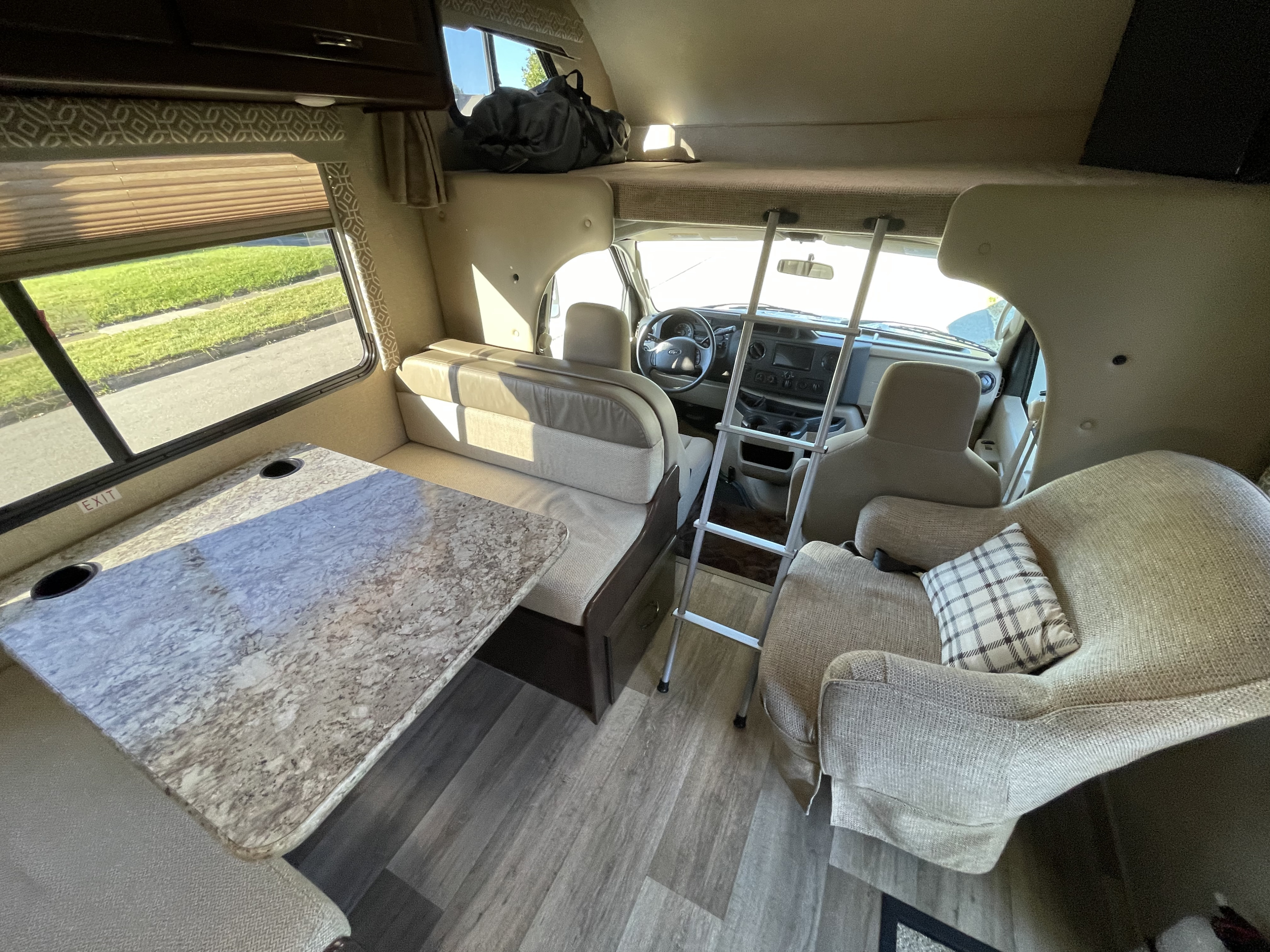 Spacious rv rental interior featuring a dinette, armchair, and an over-cab bunk bed with a ladder to the cockpit area.. Thor Freedom Elite 2017