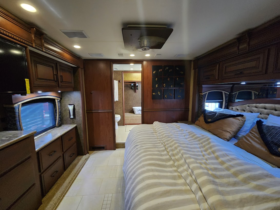 Spacious RV rental bedroom with TV, cabinetry, and private bath access. Ideal for comfortable travel.. Entegra Coach Aspire 2013