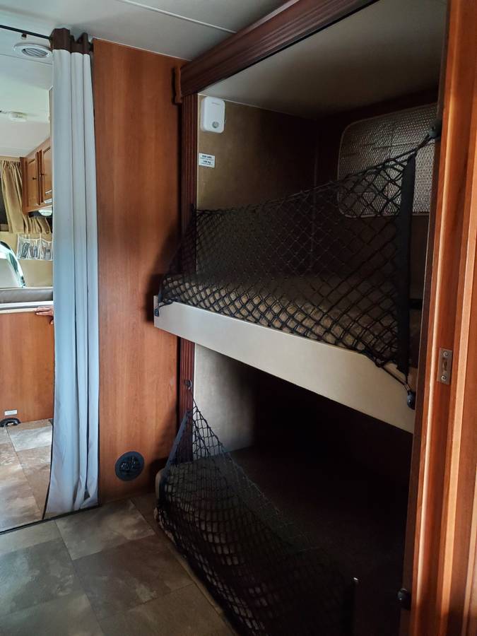 RV rental: Bunk beds with safety nets dominate this compact RV interior, with a curtain separating the sleeping area.. Coachman Leprechaun 2014