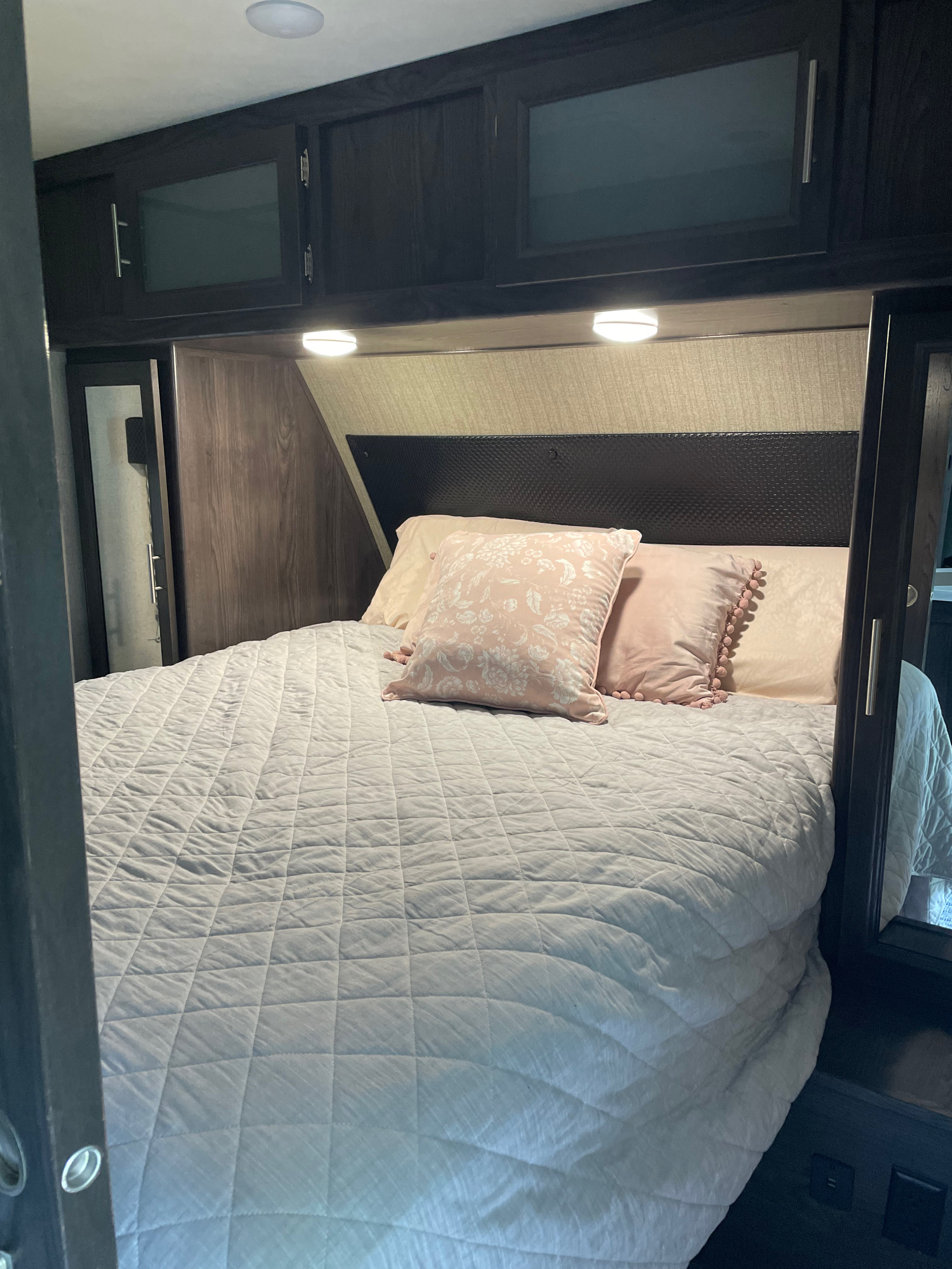 Cozy RV rental bedroom with dark cabinets, quilted bed, pink pillows, and integrated lighting.. Dutchmen Kodiak Ultimate 2018