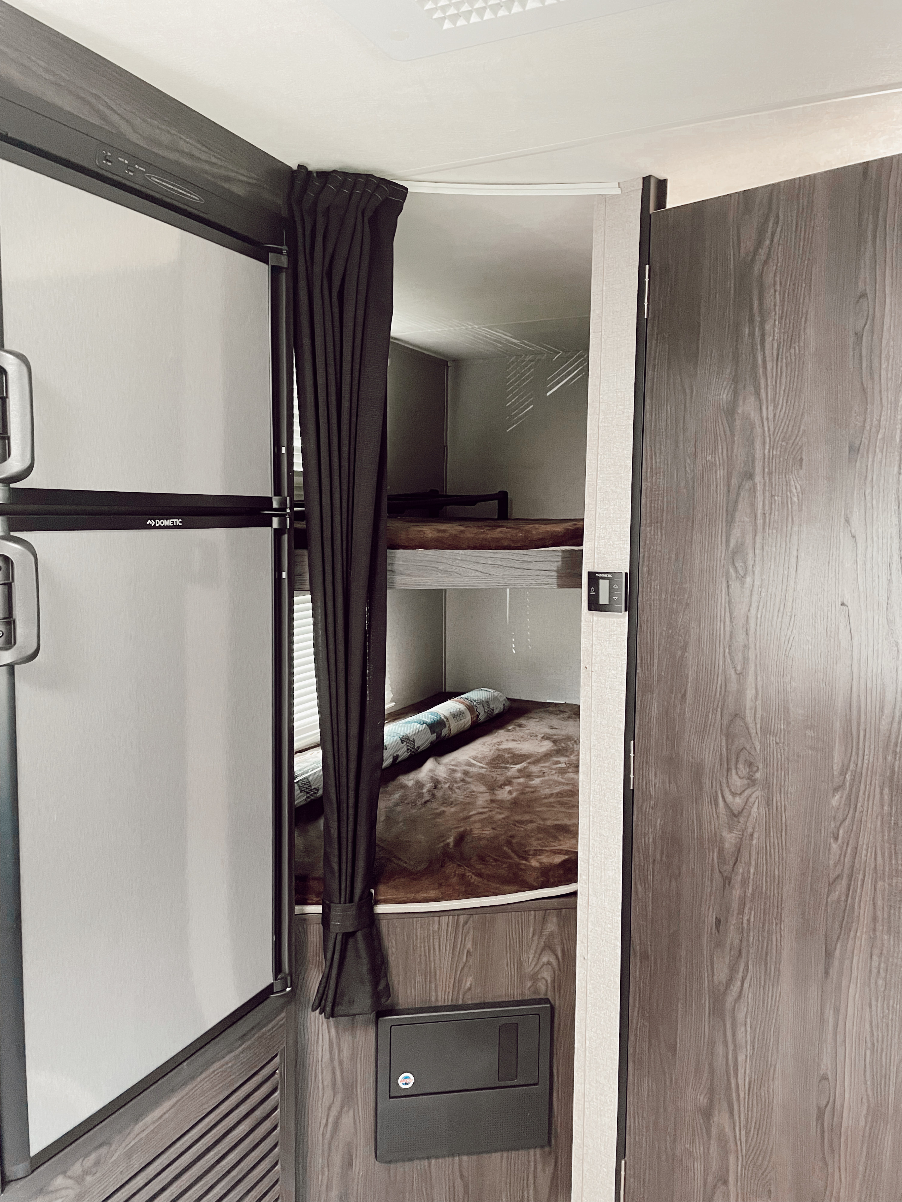 This RV rental interior features a Dometic fridge, bunk beds with curtains, and a control panel.. Dutchmen Kodiak Ultimate 2018