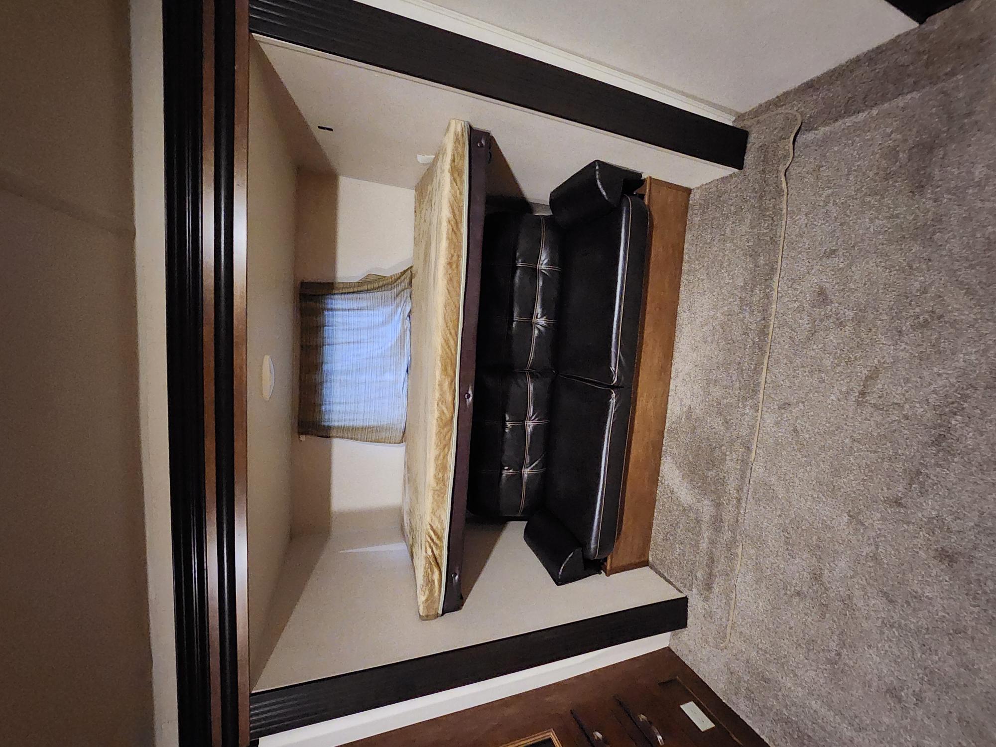 Compact RV rental living space with a wall-mounted bed, black leather sofa, and carpeted area.. Forest River Wildwood 2017