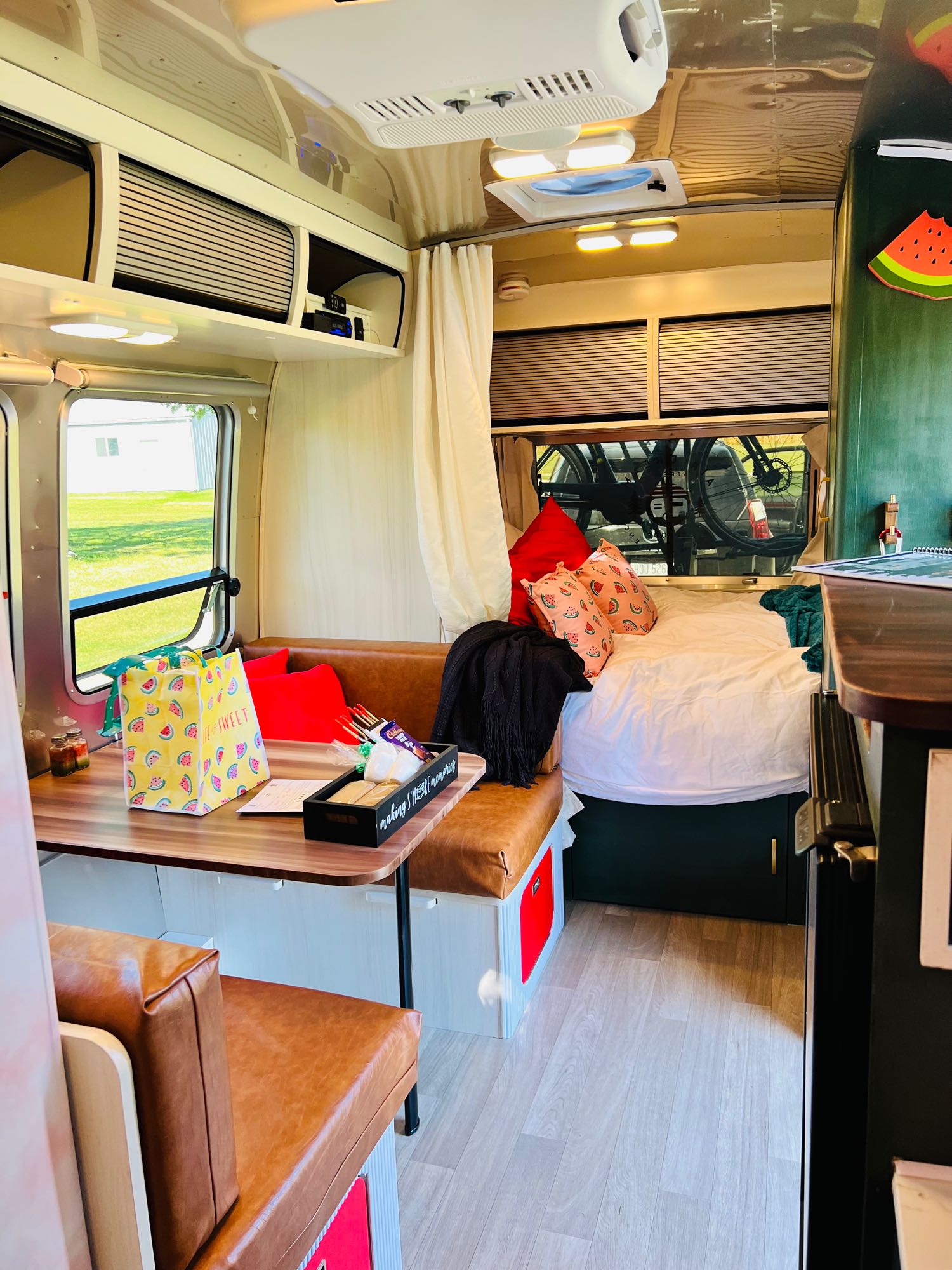 Cozy RV rental interior with bed, dining, smart storage, and fun watermelon decor for travel.. Airstream Bambi 2022
