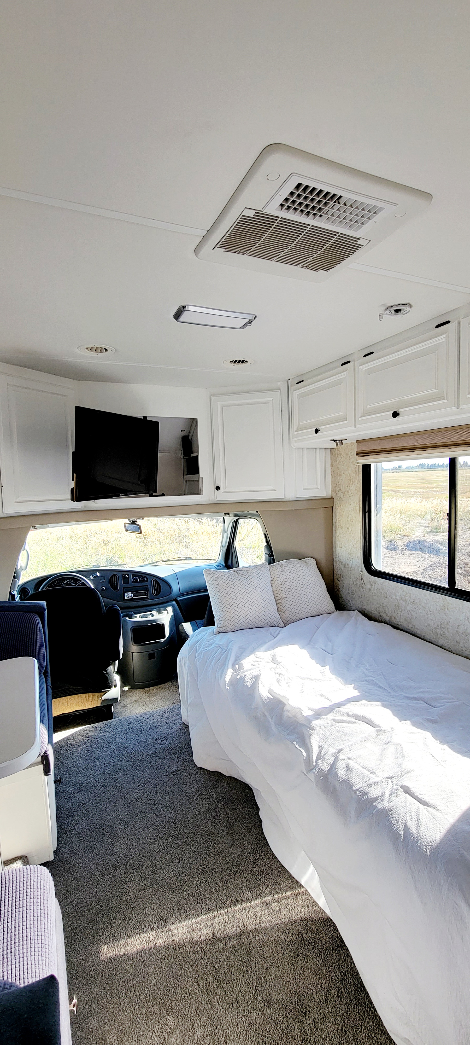 Spacious and clean RV rental interior with a cozy bed, modern cabinets, and driver's cabin. Perfect for comfortable travel.. Four Winds Siesta 2005