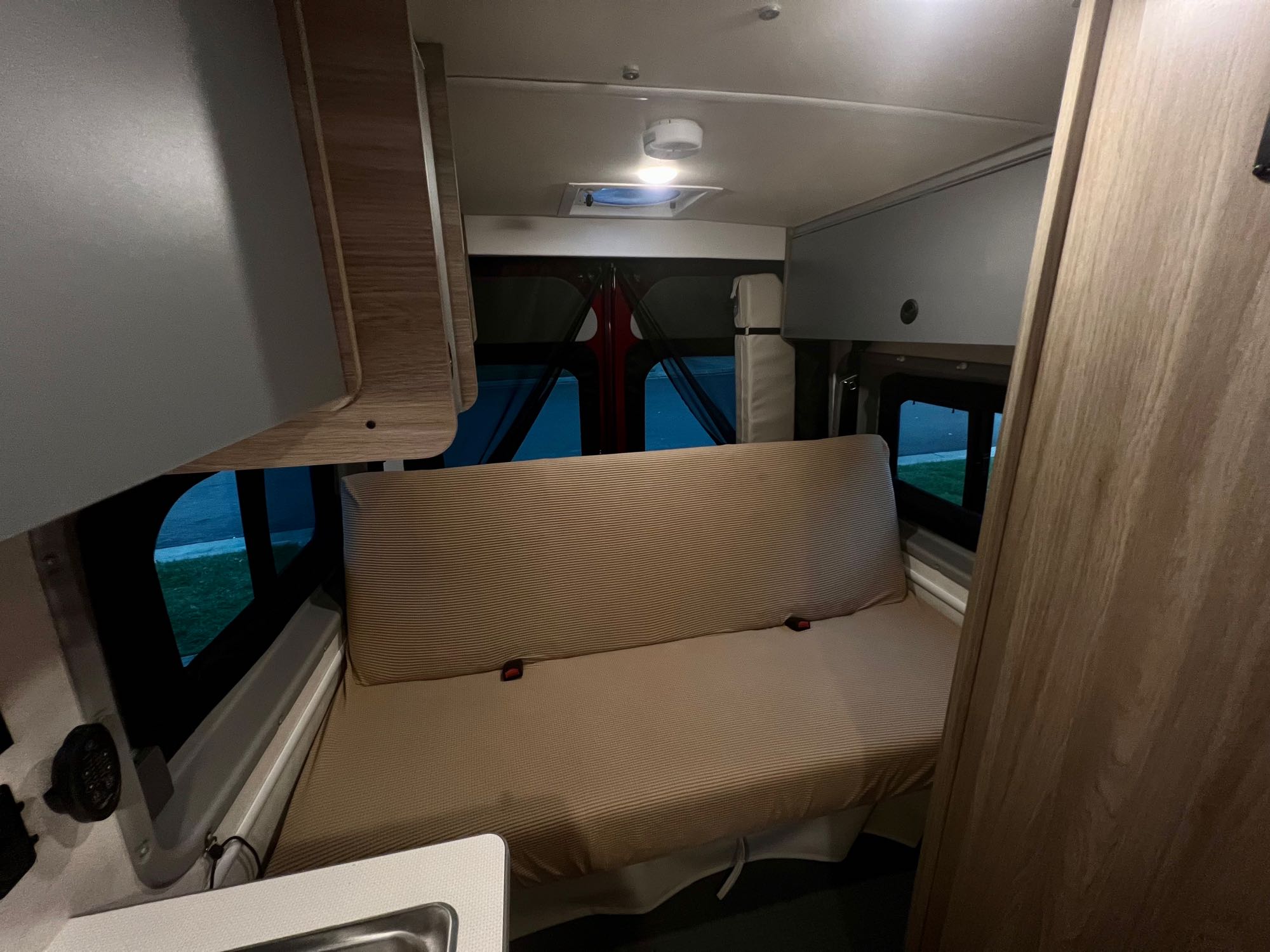 Interior of an RV rental showing a striped bench seat with seatbelts, overhead storage, and windows. Compact living space.. Winnebago Solis 2022