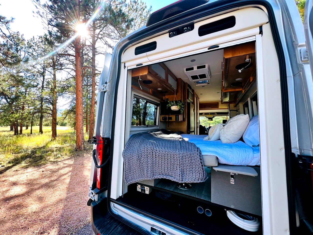 Relaxing RV rental adventure! Cozy campervan interior opens to nature, sun shining through pine trees.. Coachmen Beyond 22D 2020