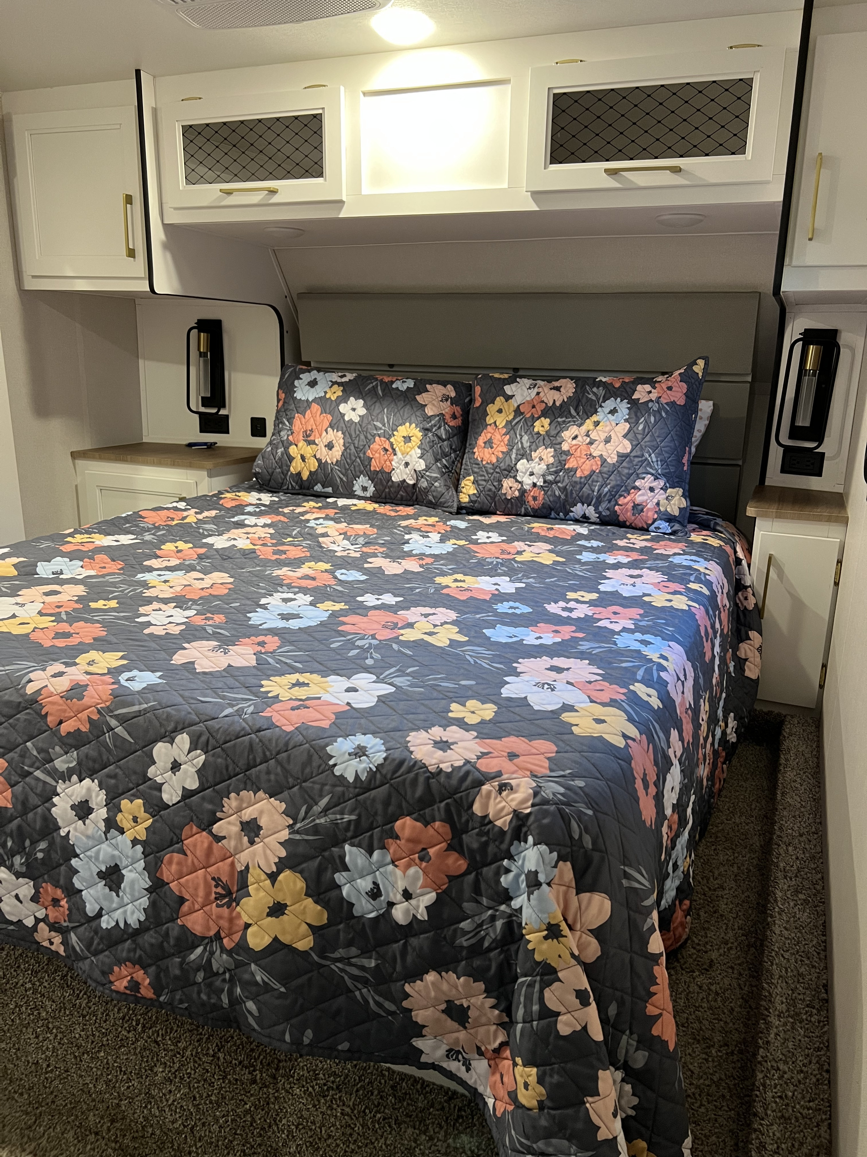 Cozy RV rental bedroom with quilted floral bedding, white cabinets, and built-in lighting.. Crusader Lite 2022