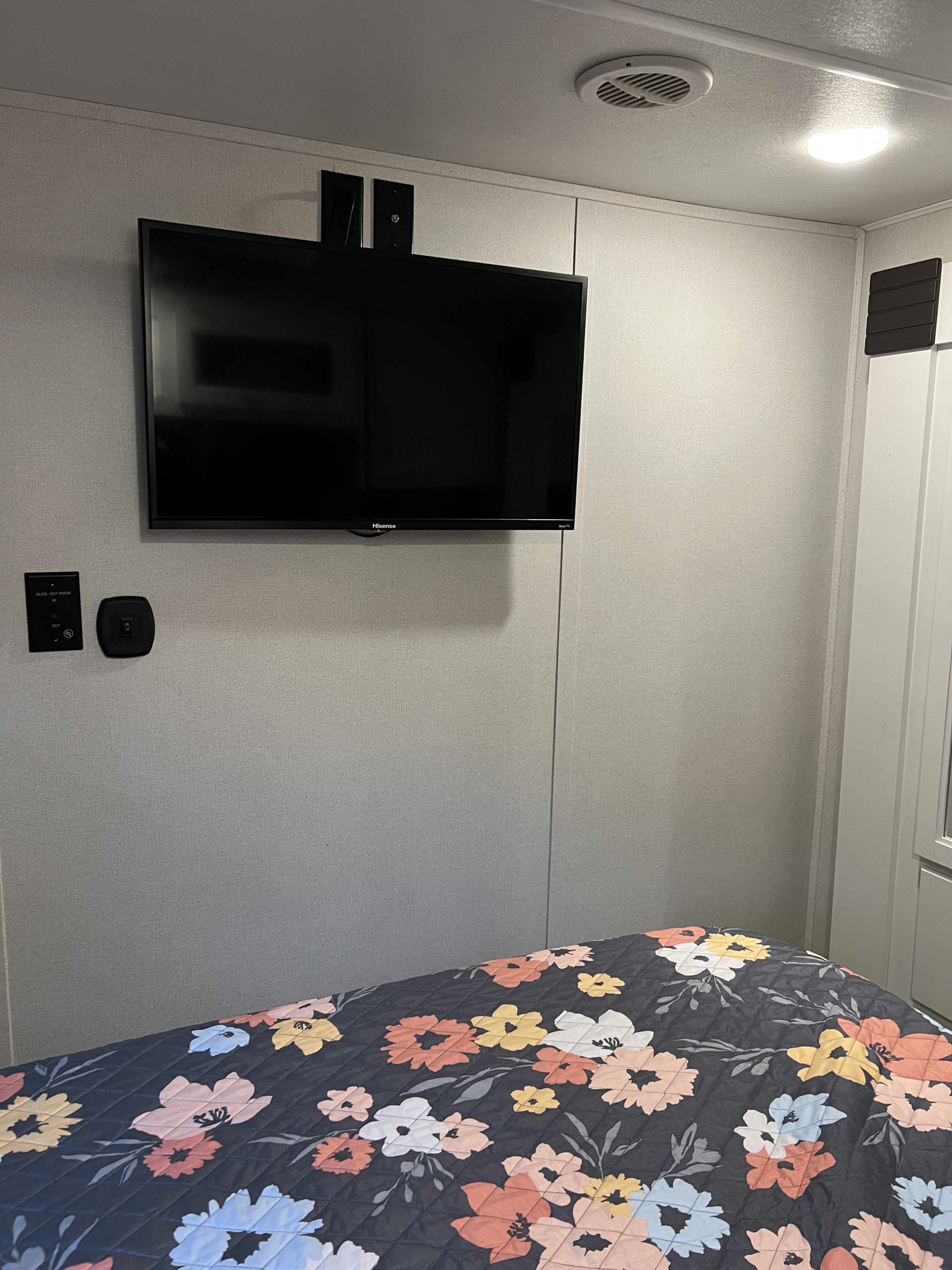Cozy RV rental bedroom featuring a wall-mounted TV, floral bed, and control panel. Ideal compact space.. Crusader Lite 2022