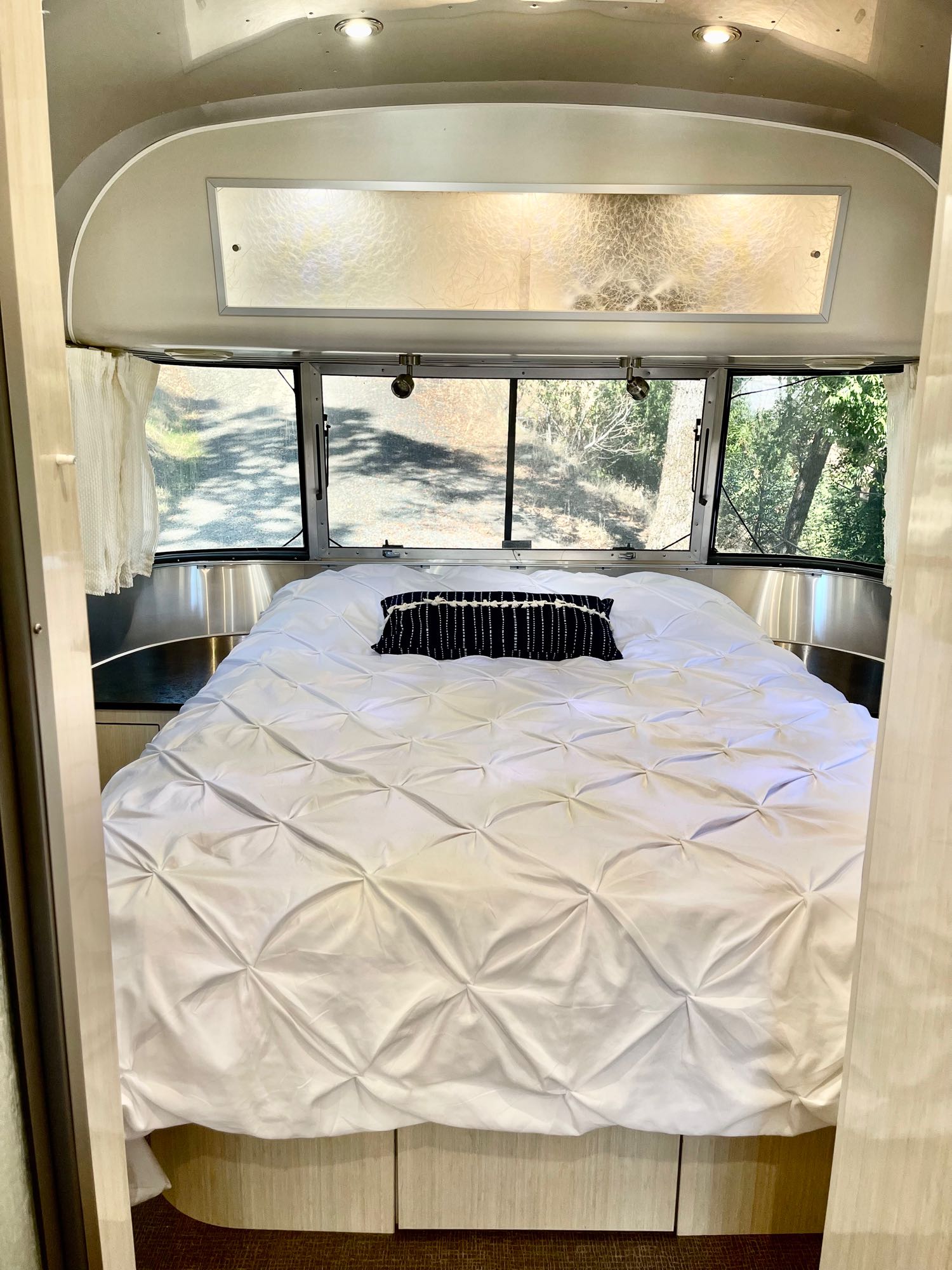 This cozy RV rental bedroom features a white tufted bed with a black pillow, large windows, and a silver interior.. Airstream International 2011