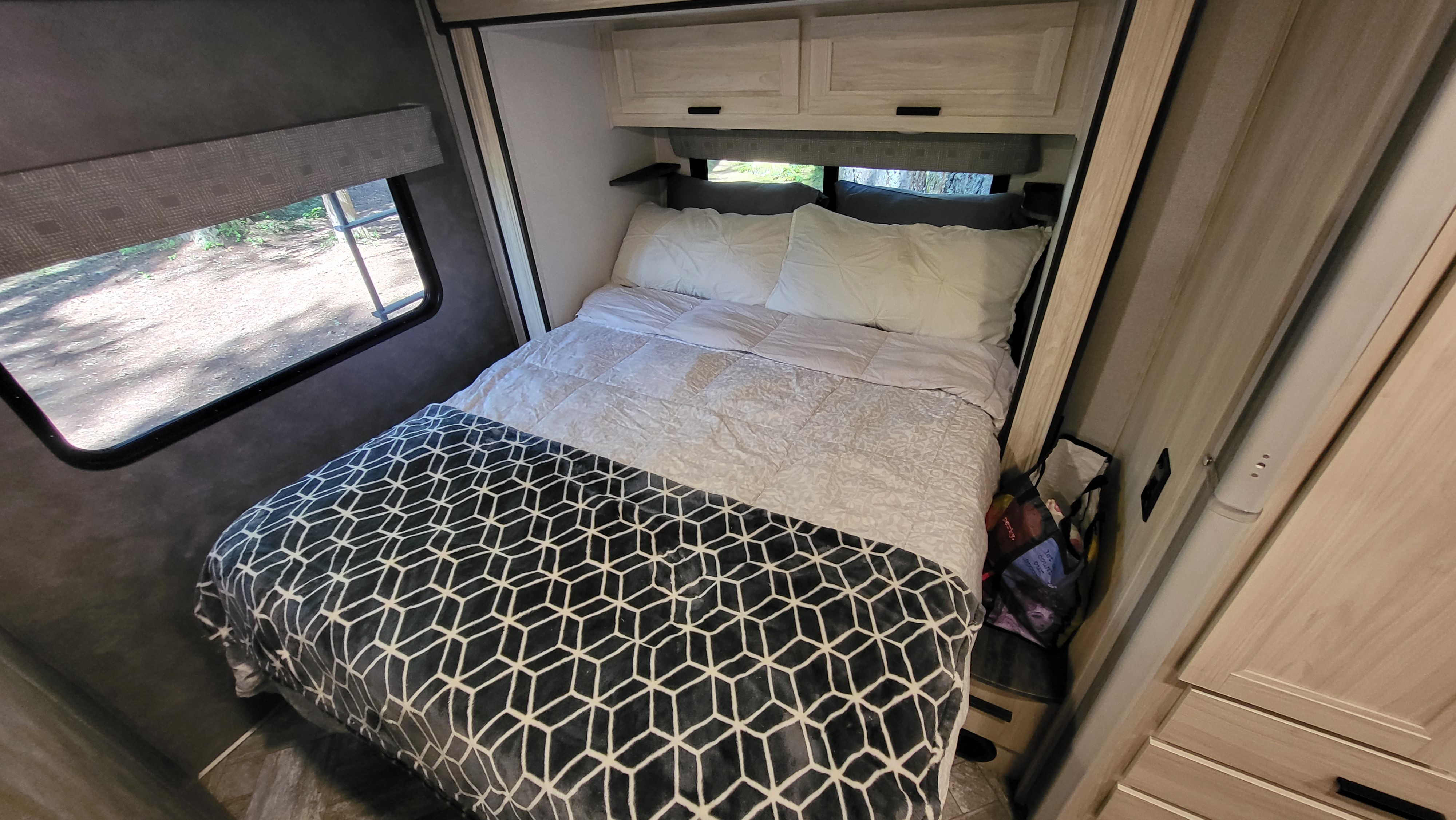 A cozy rv rental bedroom features a bed with white pillows and a black geometric blanket, plus overhead storage and a window view.. Forest River Sunseeker LE 2022