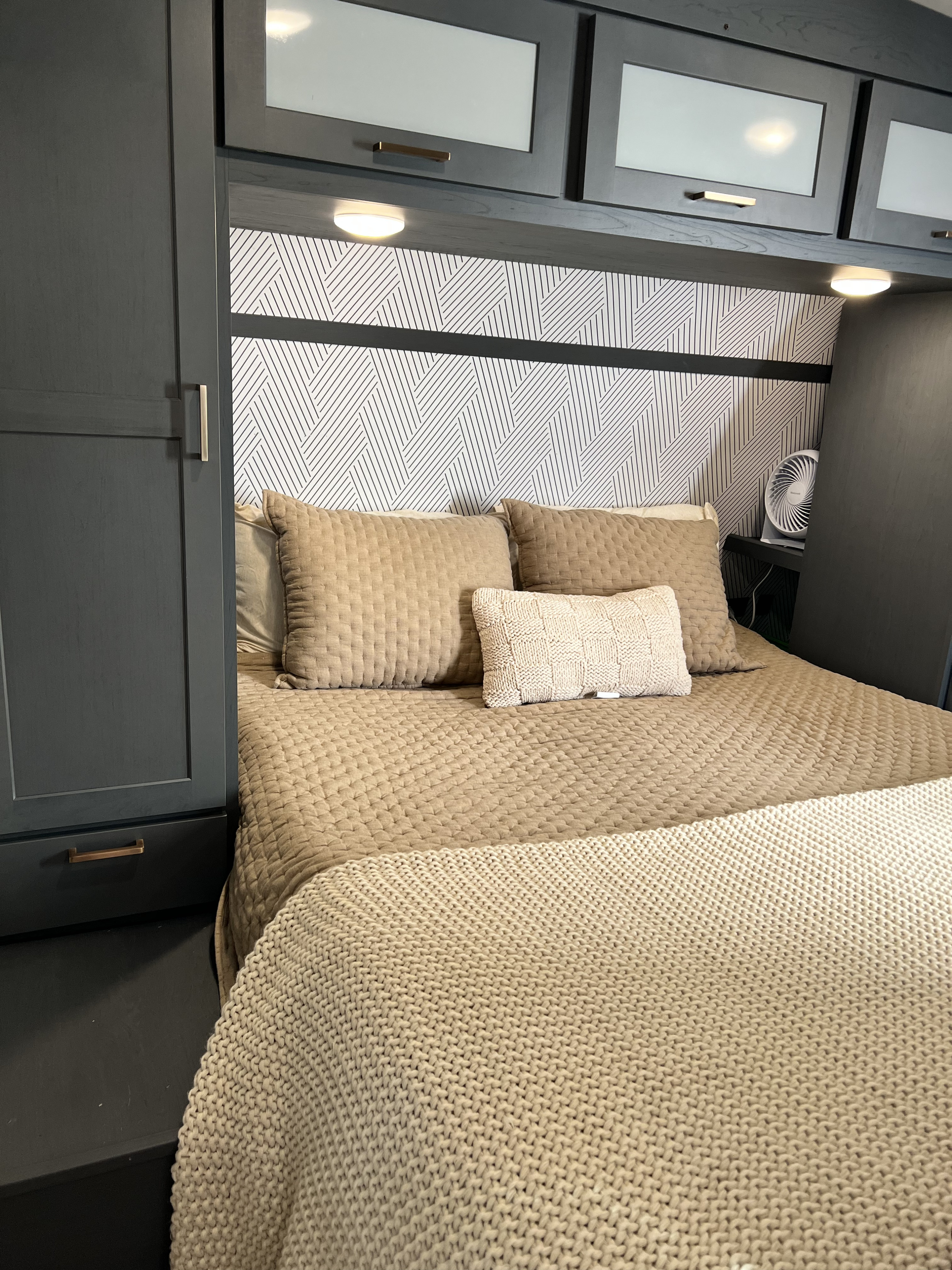 Modern RV rental sleeping area featuring dark cabinetry, geometric wallpaper, and comfortable neutral bedding.. Keystone RV Bullet Ultra Lite 2022