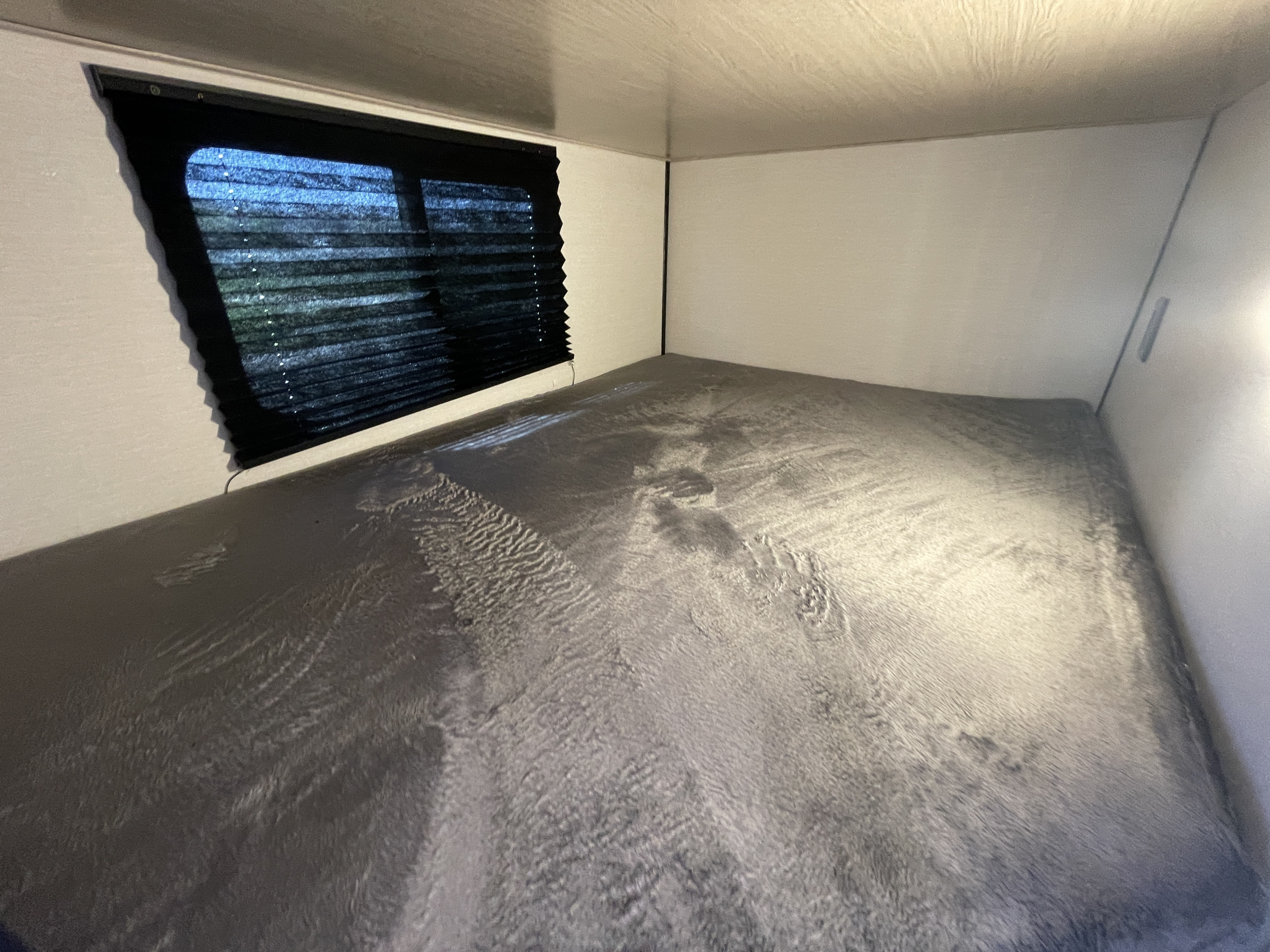 Compact RV rental sleeping area: a comfortable bed with a gray textured blanket and window with closed blinds.. Coachmen Apex 2022