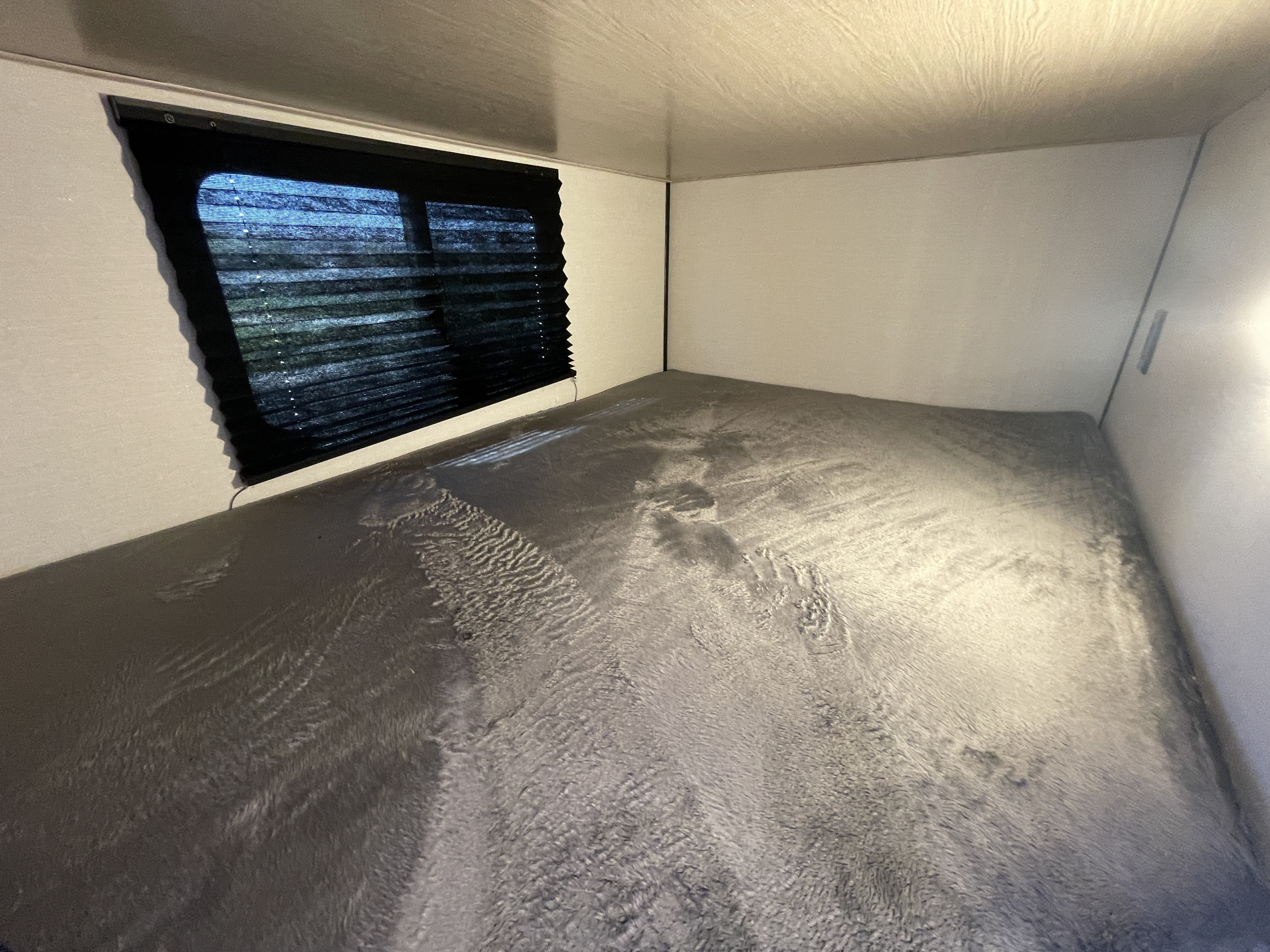 Cozy RV rental bunk bed with soft gray blanket, window, and pleated blinds for a comfortable sleeping area.. Coachmen Apex 2022