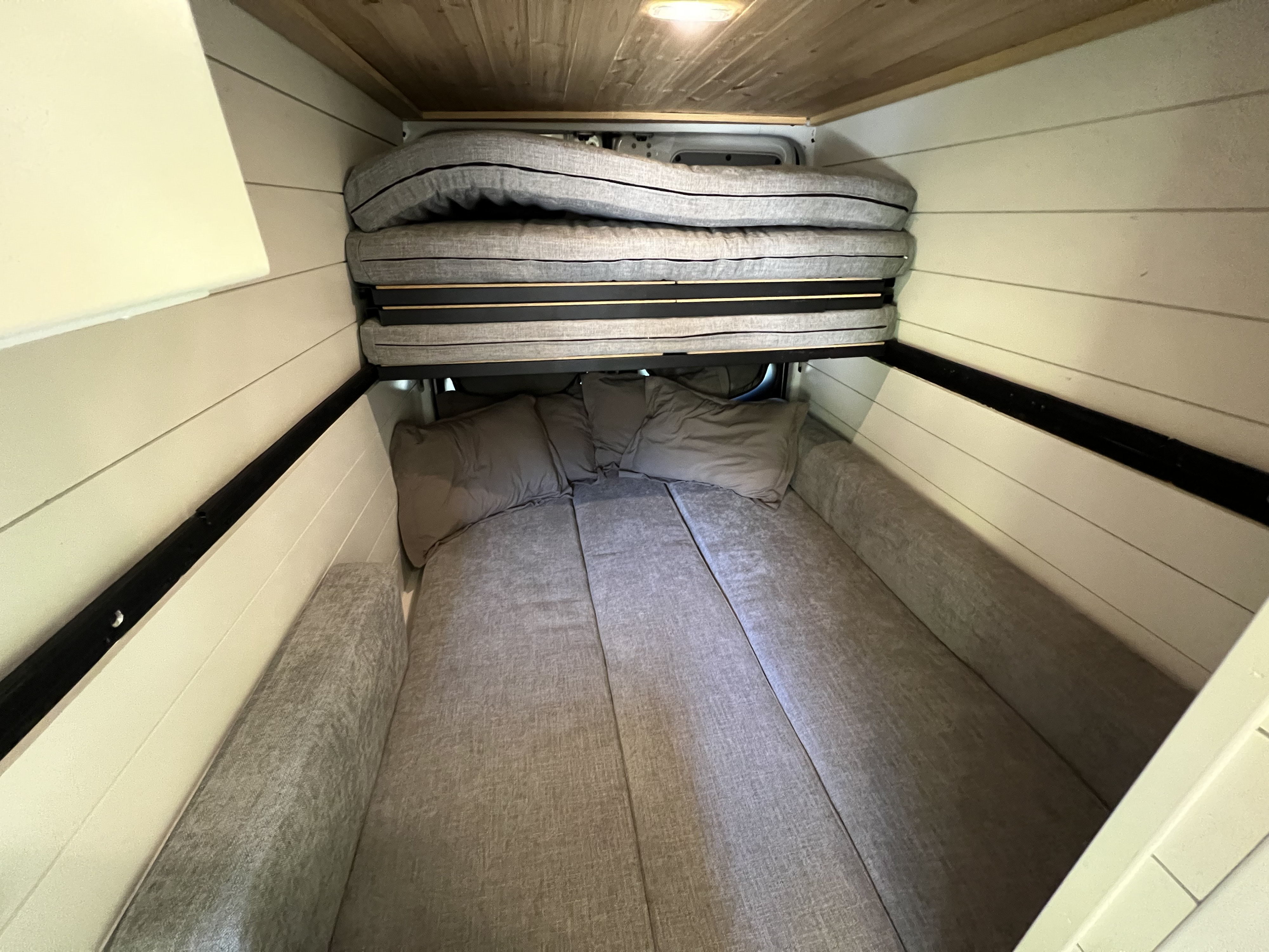 Inside an RV rental: a cozy, convertible bed setup. Lower cushions form a bed, with upper cushions folded neatly.. Mercedes-Benz Sprinter 2020