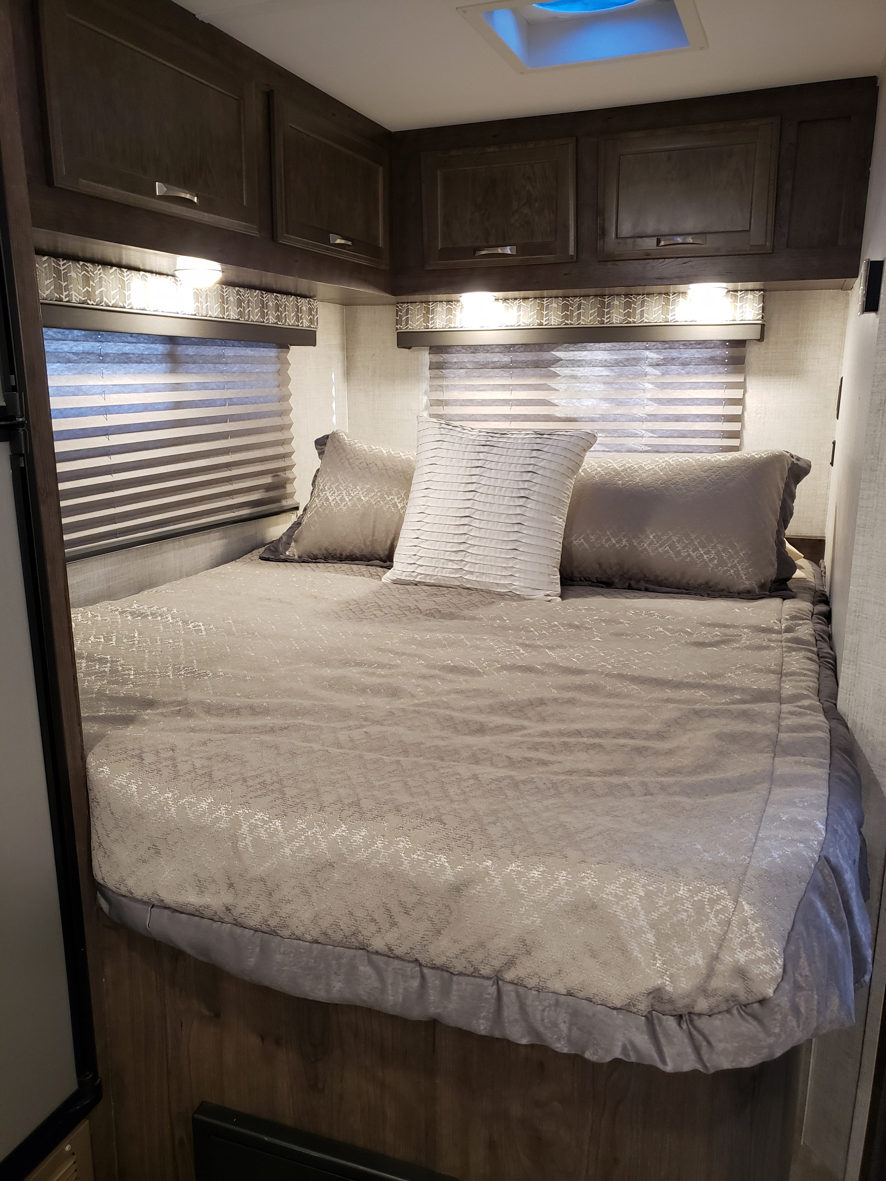 Cozy RV rental bedroom featuring a queen bed with patterned bedding, overhead cabinets, soft lighting, and pleated blinds.. Gulf Stream Conquest 2022