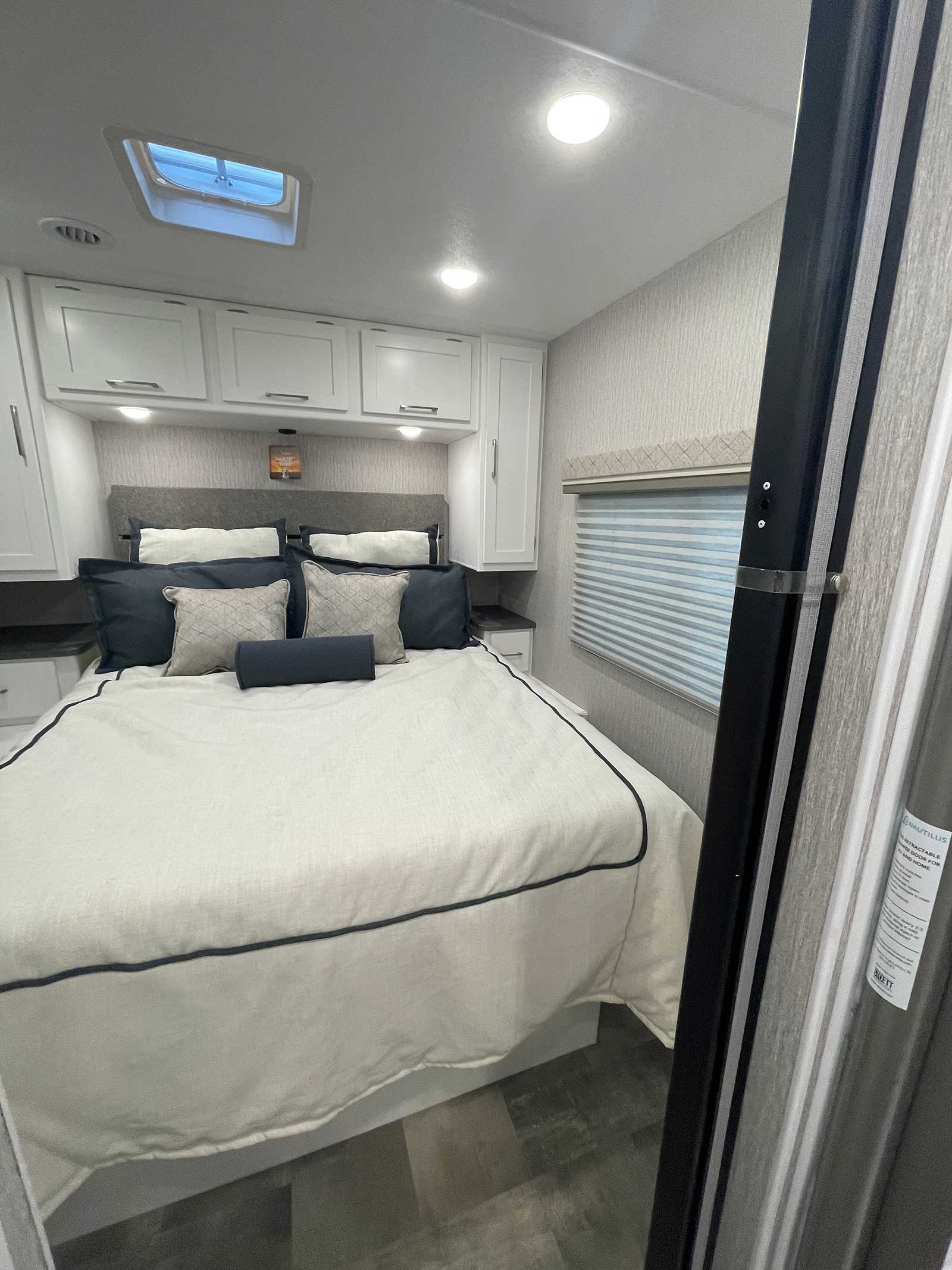 Spacious & modern RV rental bedroom featuring a comfy bed, skylight, overhead cabinets, and nightstands for your travels.. Coachmen Pursuit 2023