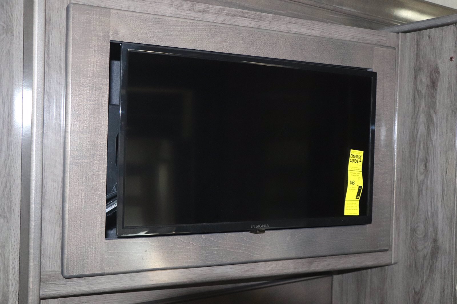 An Insignia TV with an Energy Guide sticker is mounted in light wood cabinetry, offering entertainment in an rv rental.. Fleetwood Bounder 2024
