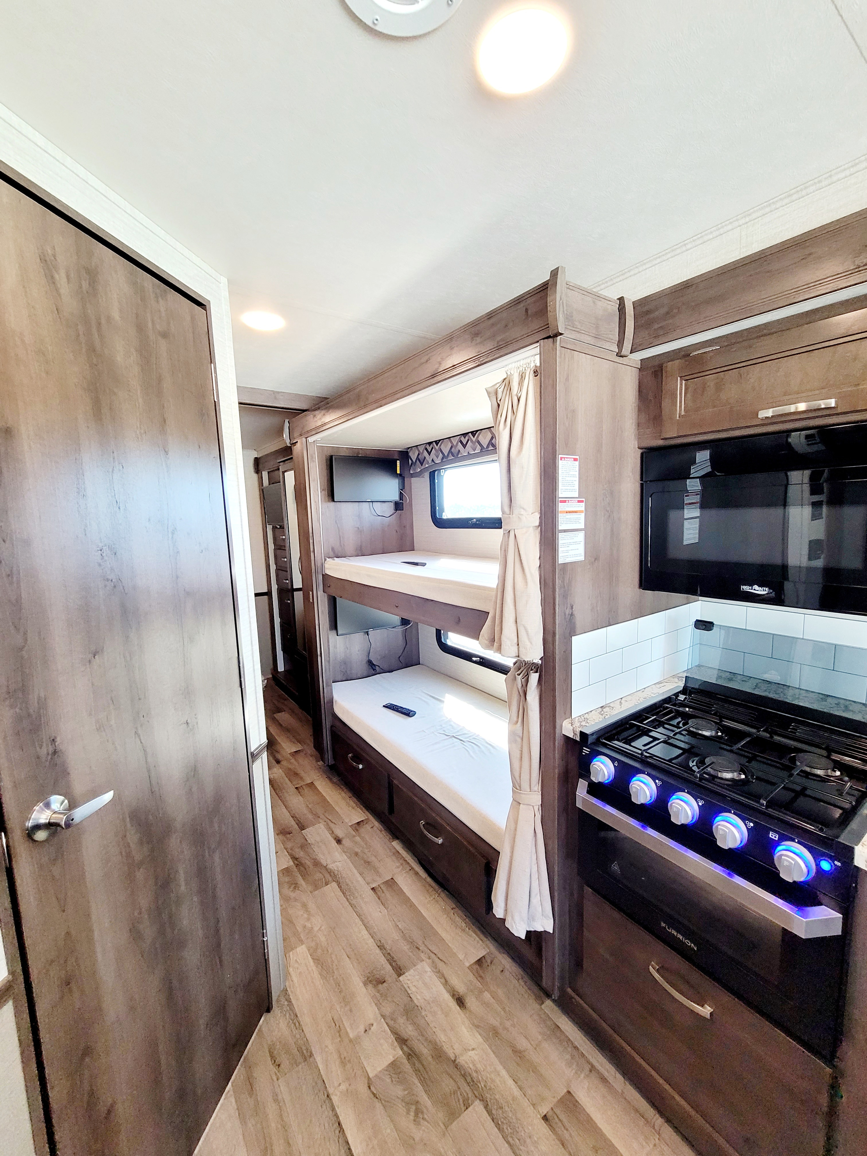 Modern RV rental interior with a functional kitchen featuring a stove and microwave, plus cozy bunk beds with a TV.. Jayco Alante 2020