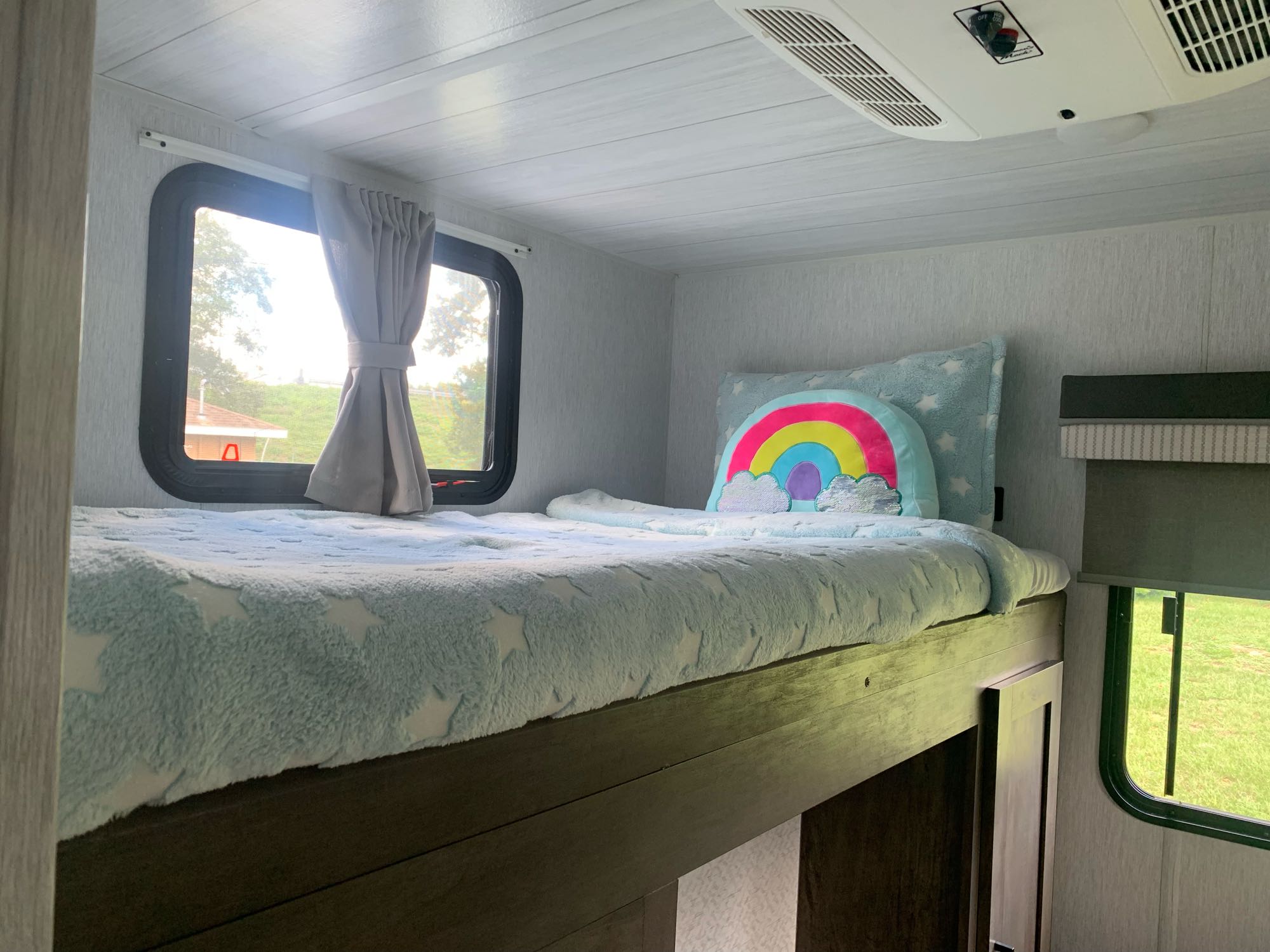 Cozy RV rental bunk bed setup with a fuzzy star blanket, rainbow pillow, and scenic window view.. Forest River Salem 2022