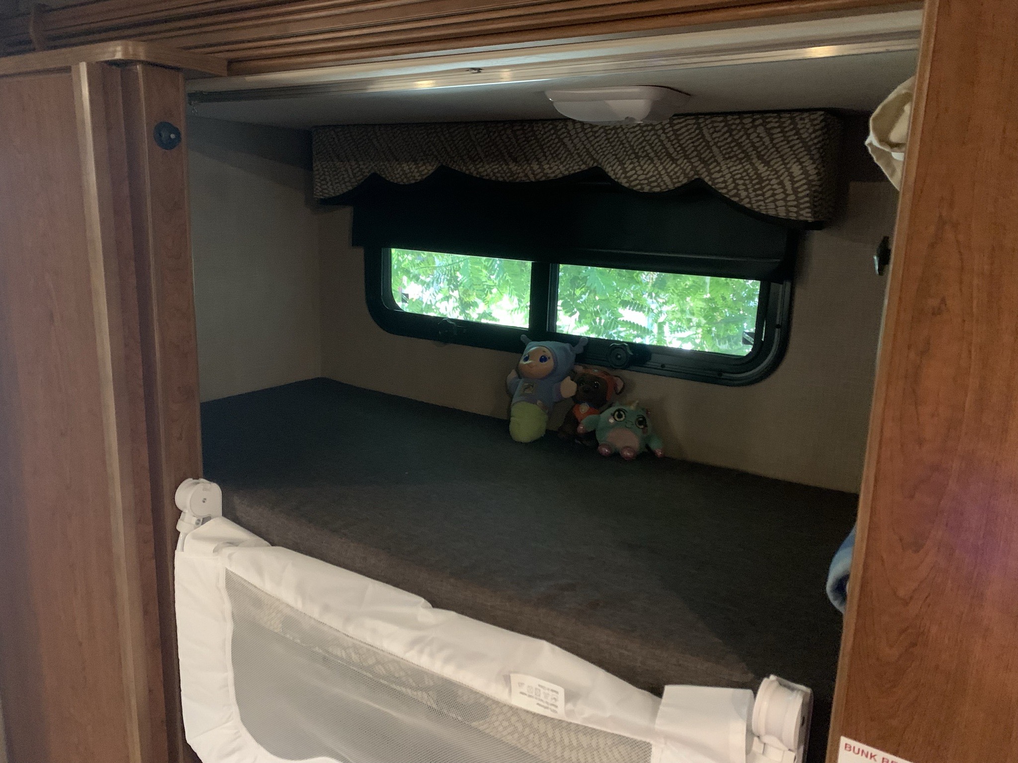 Cozy RV rental bunk bed with a child safety rail, window view, and plush toys for a comfortable stay.. Holiday Rambler Vacationer 2017