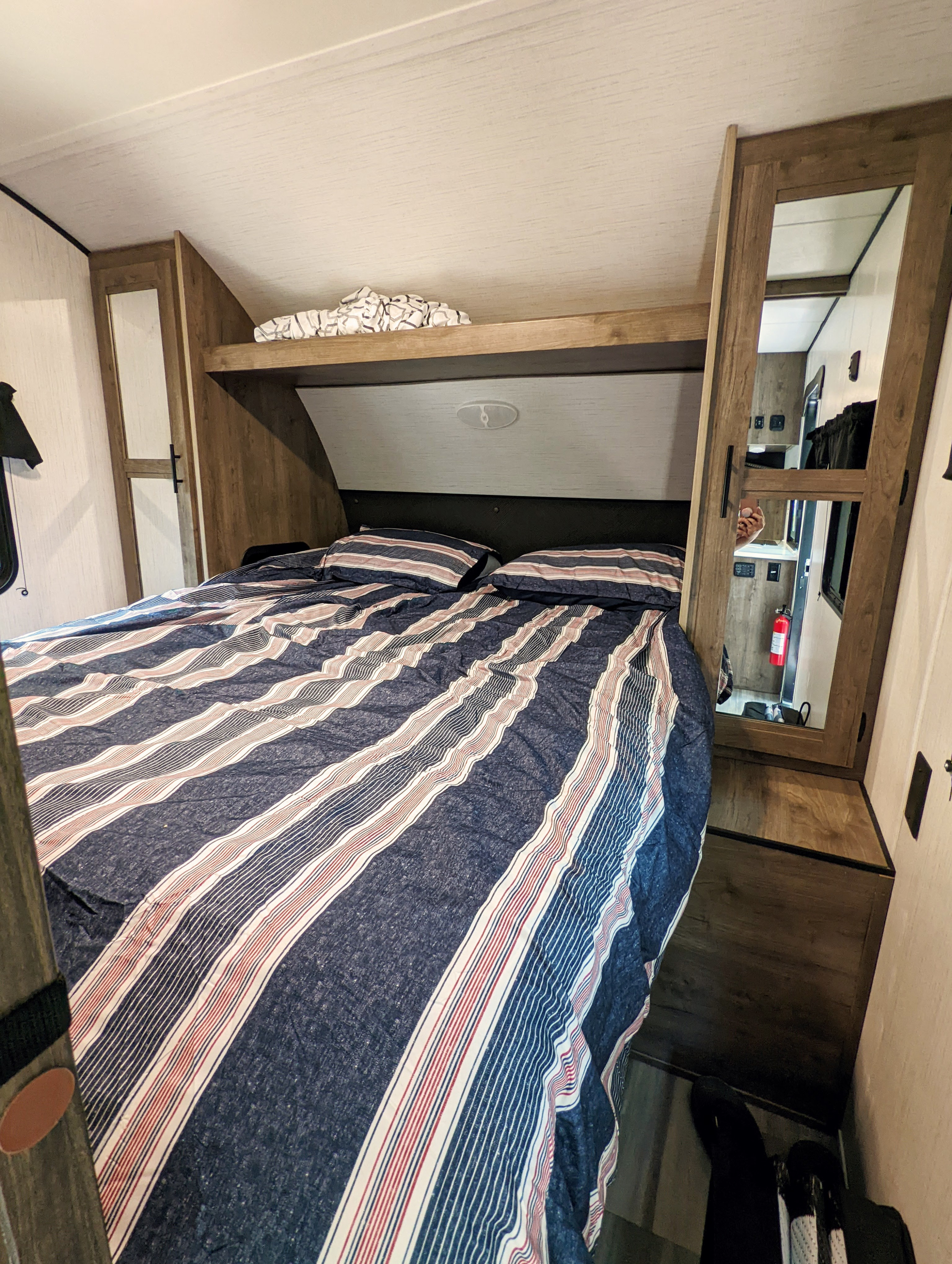 Explore this inviting RV rental bedroom. Features a comfortable striped bed, overhead storage, and mirrored closet doors.. Heartland RVs Pioneer 2022