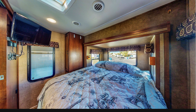 Cozy RV rental bedroom with a large bed (Eiffel Tower comforter), TV, and windows showing outdoor scenery.. Forest River Sunseeker MBS 2016