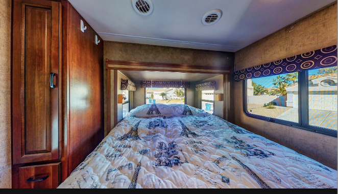 Cozy RV rental bedroom with Eiffel Tower bedding, built-in storage, and bright windows showing a desert view.. Forest River Sunseeker MBS 2016