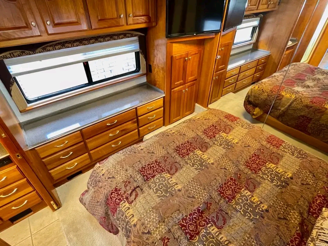 Experience comfort in this RV rental bedroom: large bed with patterned comforter, wood storage, and a mirrored wall.. Country Coach Allure 2004
