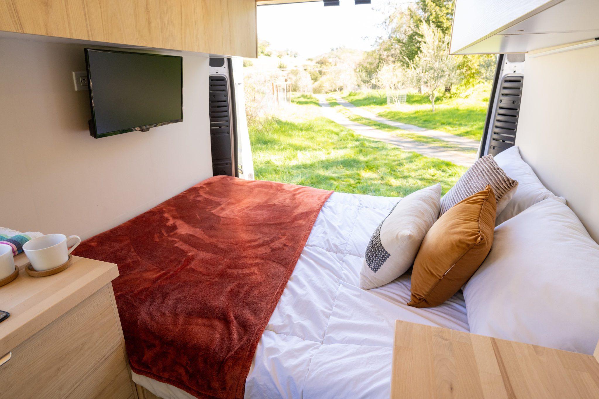 Cozy RV rental interior: comfortable bed, TV, & scenic outdoor view through open doors.. ram ProMaster 2021