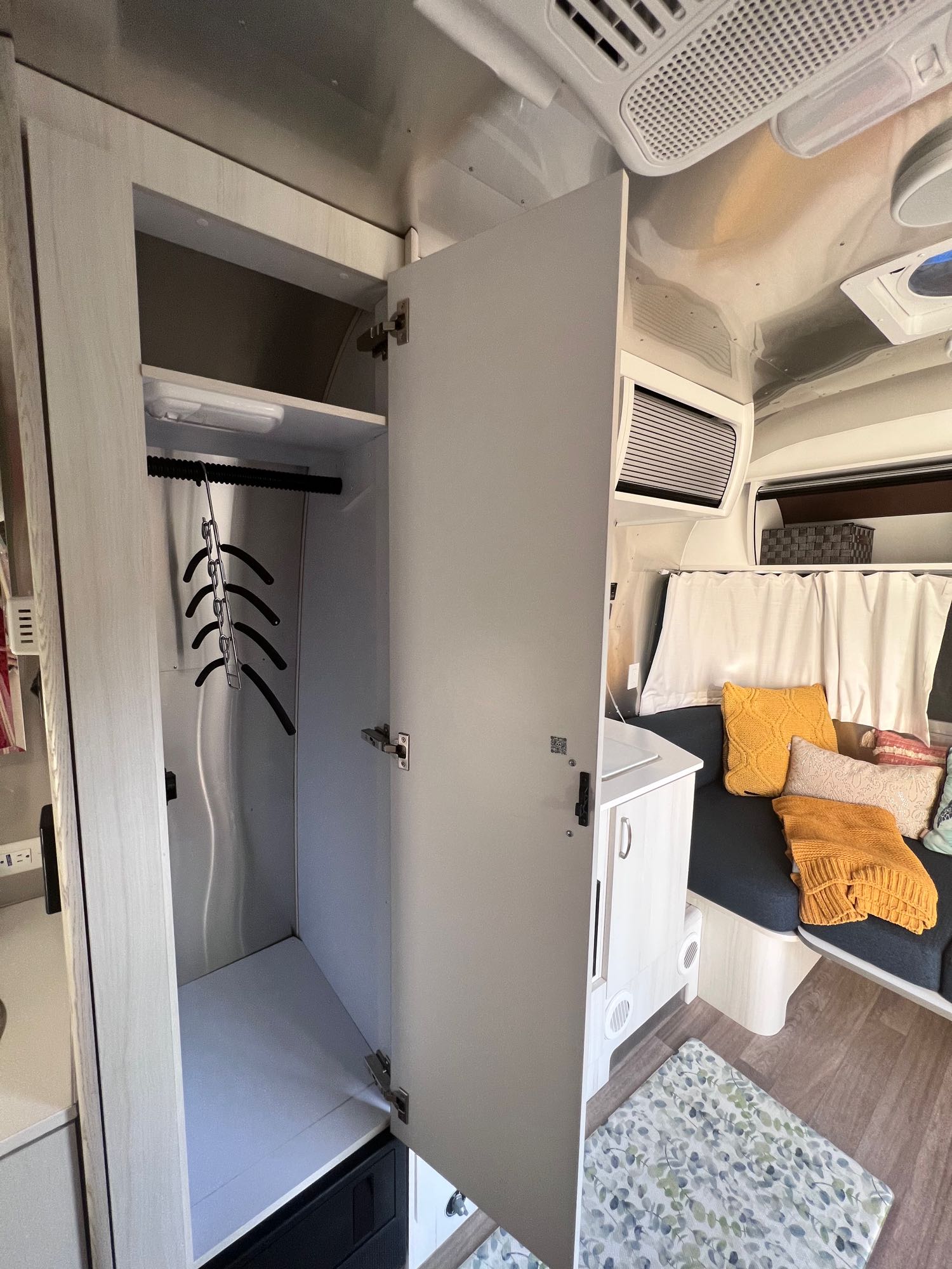 Inside this RV rental, an open wardrobe provides hanging space, next to a comfy couch with bright pillows.. Airstream Bambi 2022