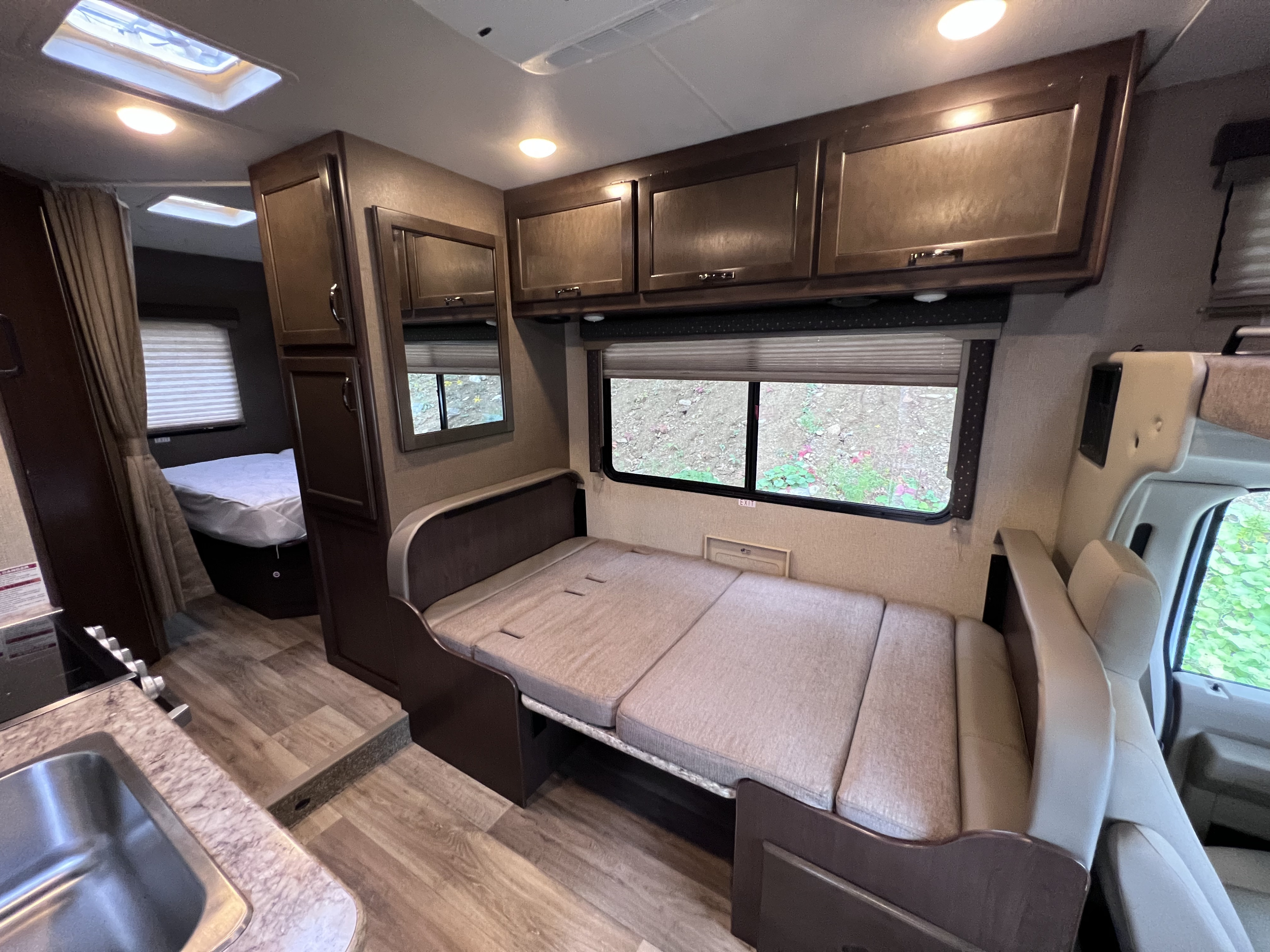 Inside an RV rental: view of the dinette seating that converts to a bed, overhead storage, kitchen sink, and rear sleeping area.. Thor Freedom Elite 2018
