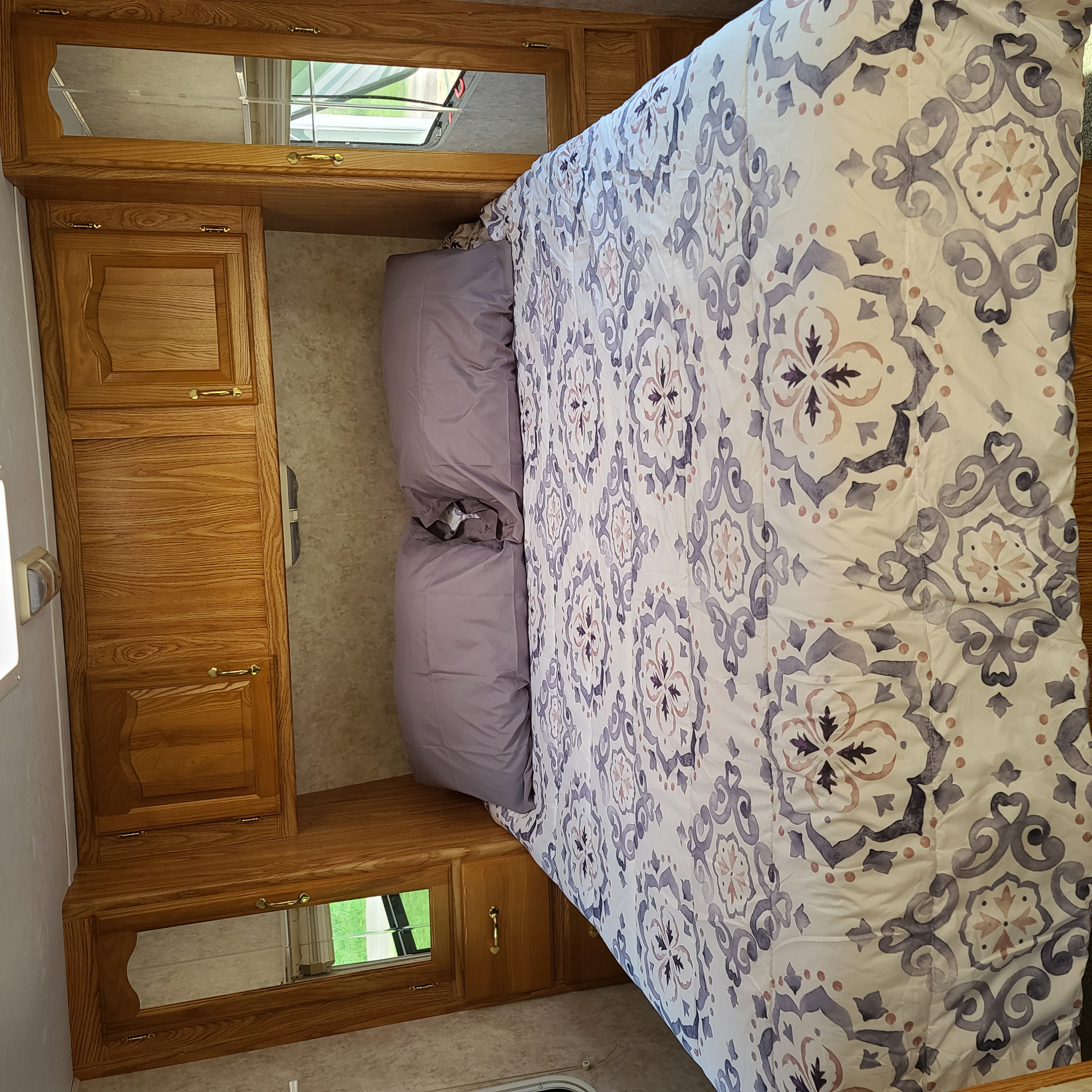 RV rental interior: cozy bedroom with a patterned comforter, lavender pillows, and built-in oak cabinets/storage.. Cedar Creek Cedar Creek Fifth Wheel 2005