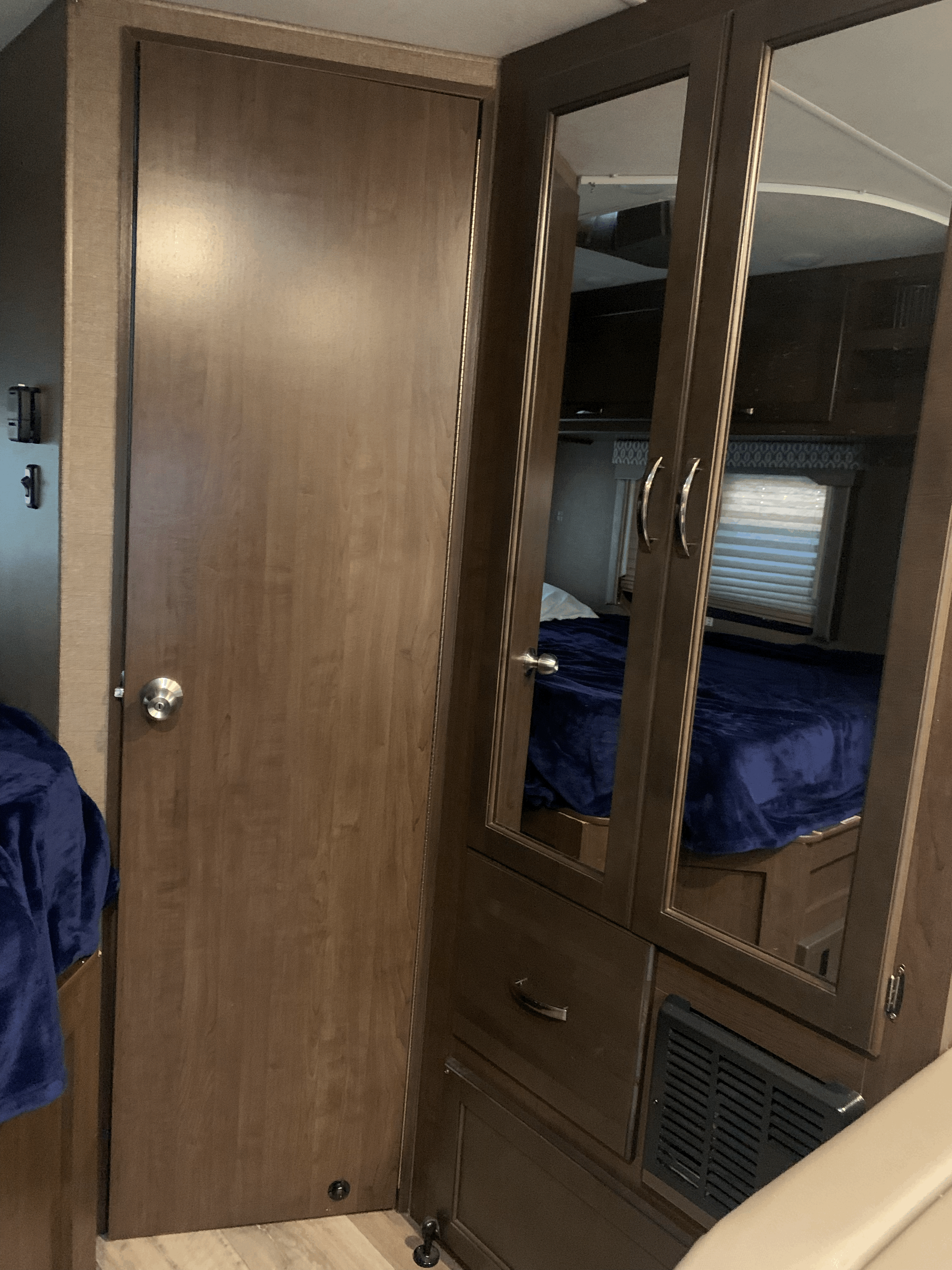 Cozy RV rental interior featuring a wooden door and mirrored closet, reflecting the bedroom with a blue blanket and window.. Thor Freedom Elite 2019