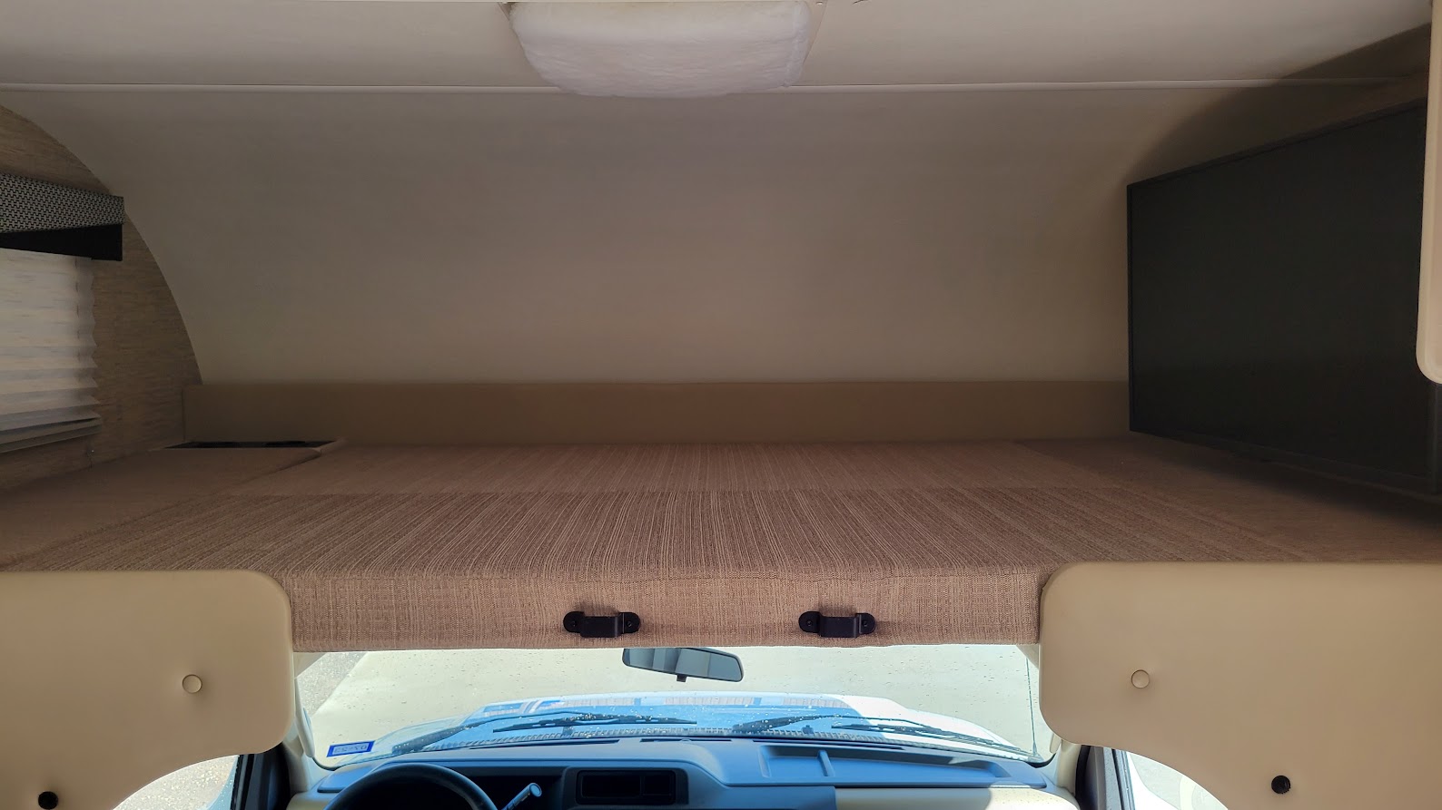 RV rental overhead bunk interior, showing the textured bed above the cab, dashboard, and a TV.. Thor Freedom Elite 2022