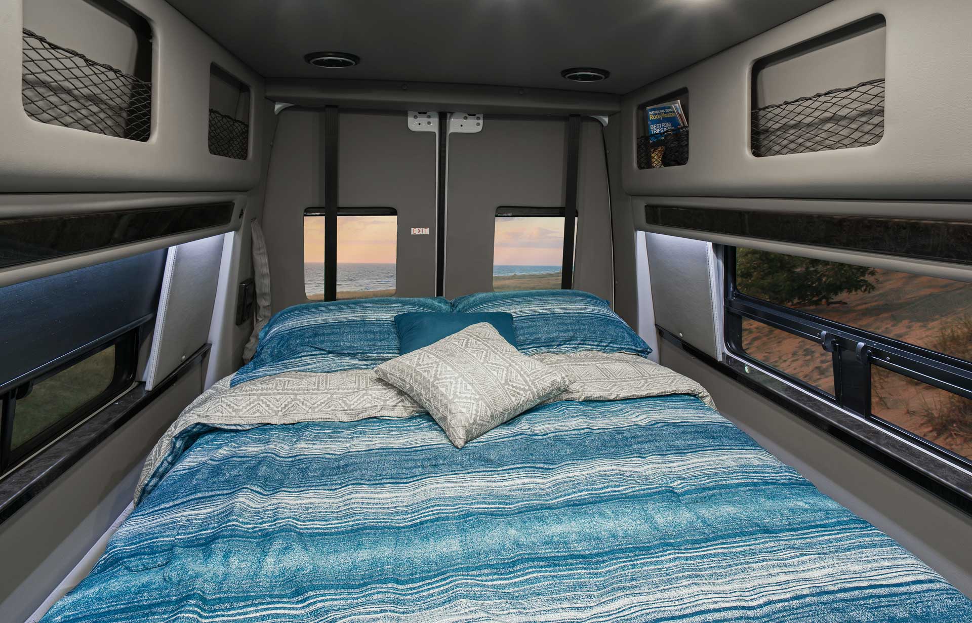 RV rental bedroom features a cozy bed, side windows with ocean & sandy views. Perfect for travel adventures.. Midwest Automotive Designs Midwest Automotive Designs Class B 2021