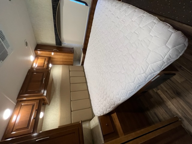 Comfortable RV rental bedroom featuring a large white quilted mattress, rich wood cabinets, and built-in seating for storage.. Coachman Mirada 2018