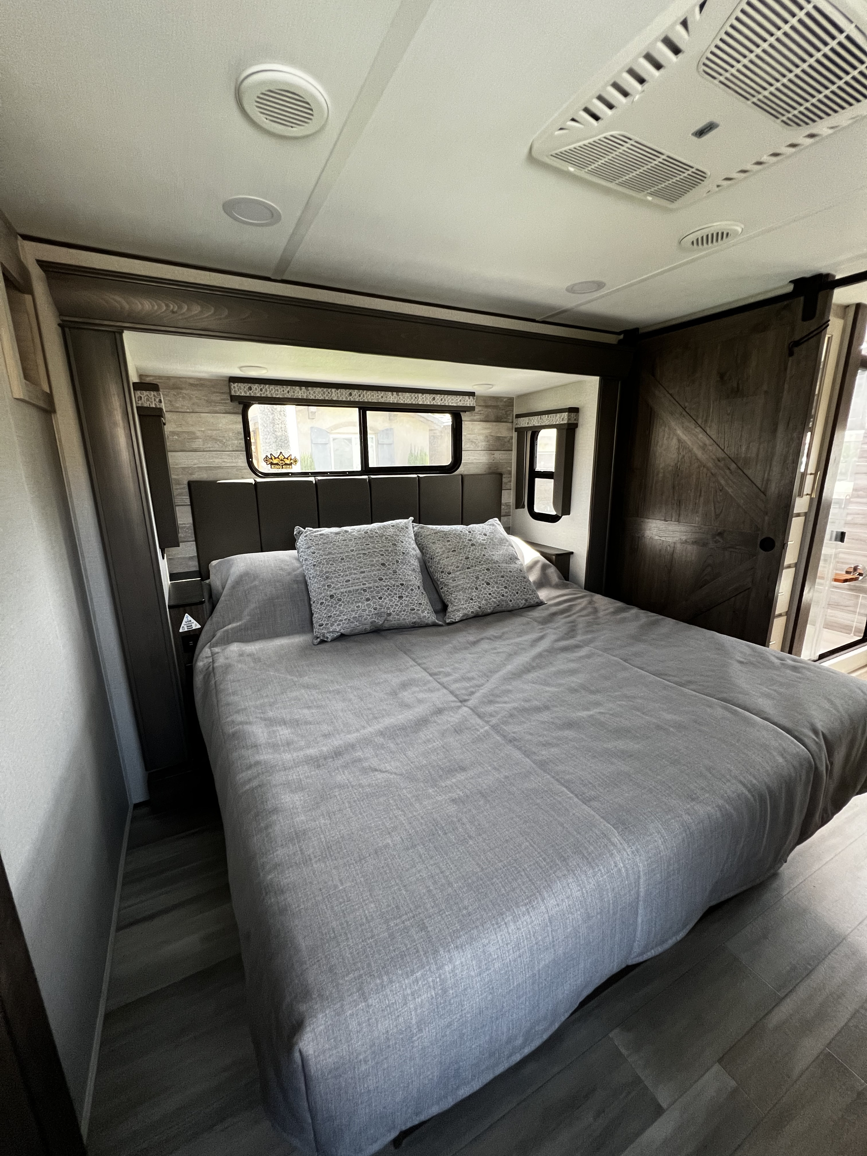 Comfortable RV rental bedroom with modern grey decor, sleek barn door, and ample light. Ideal for travel.. Alliance RV Paradigm 2021
