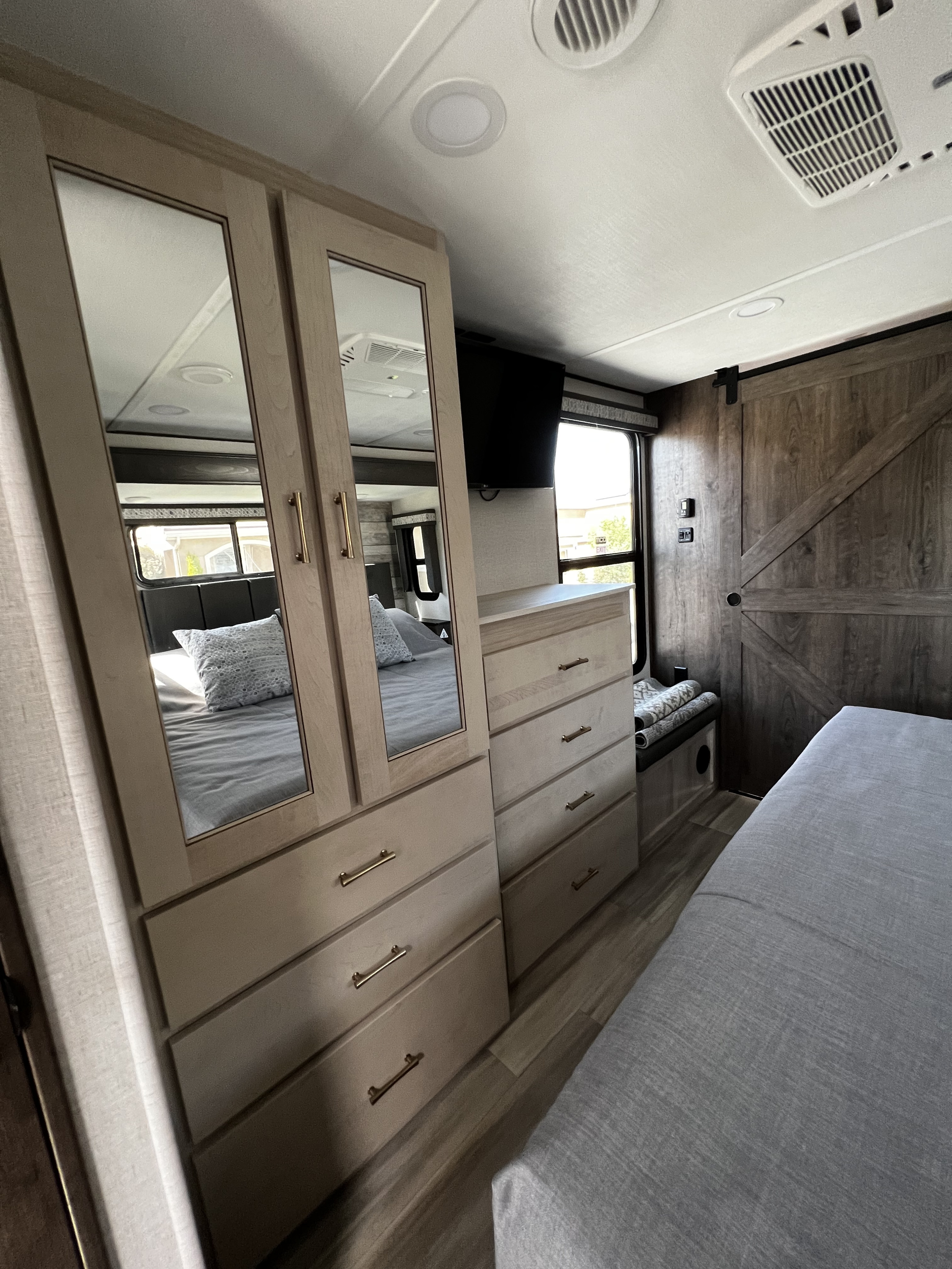 Explore this RV rental bedroom's amenities: mirrored closet, dresser, TV, and a barn door, designed for comfort and storage.. Alliance RV Paradigm 2021