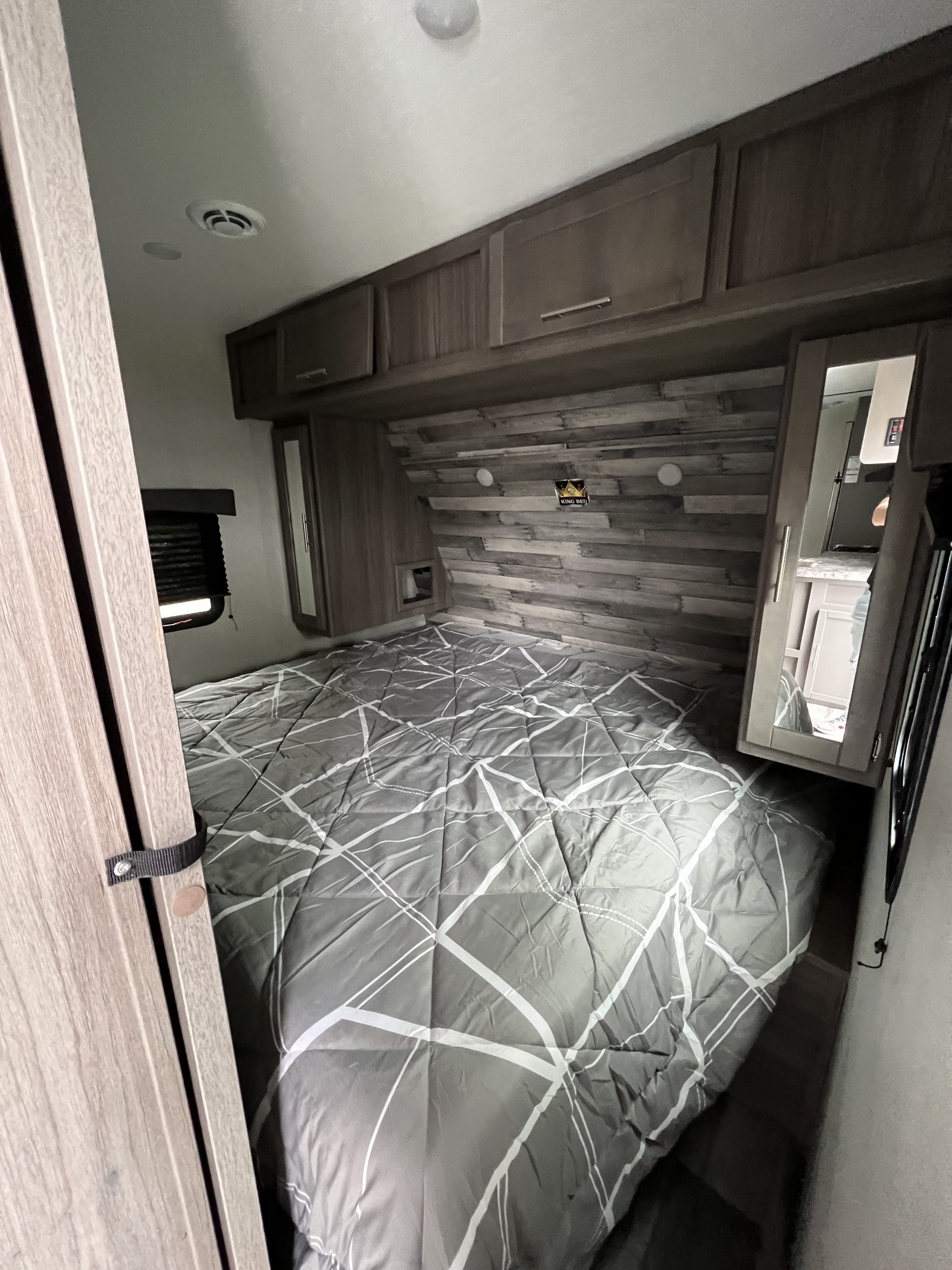 Step into comfort! This RV rental bedroom features a king bed with modern comforter, built-in storage, and wood accents.. Crossroads RV Volante 2022