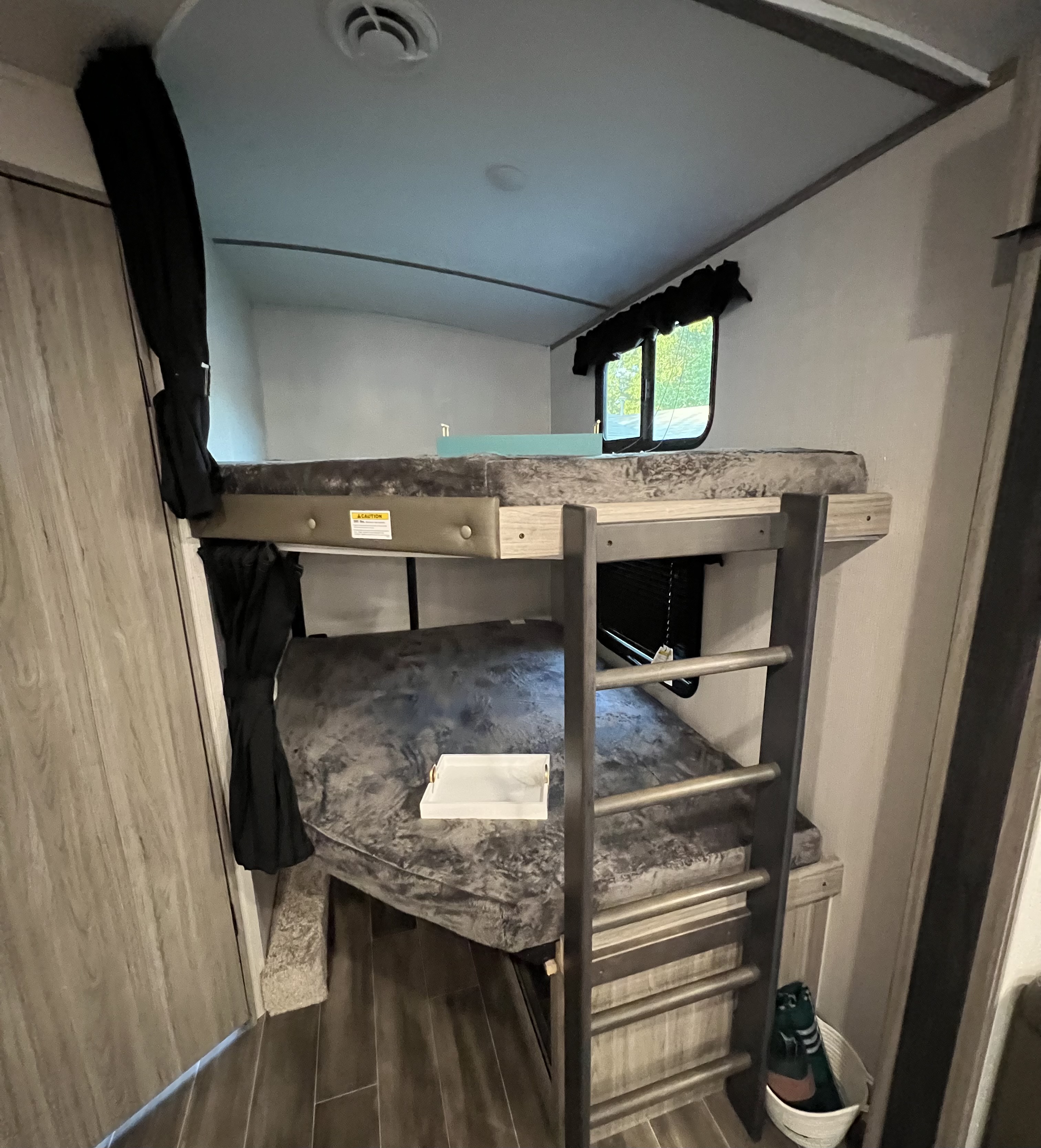 Cozy bunk beds in an RV rental, complete with dark grey bedding, a ladder, and a window view.. Keystone Passport 2022