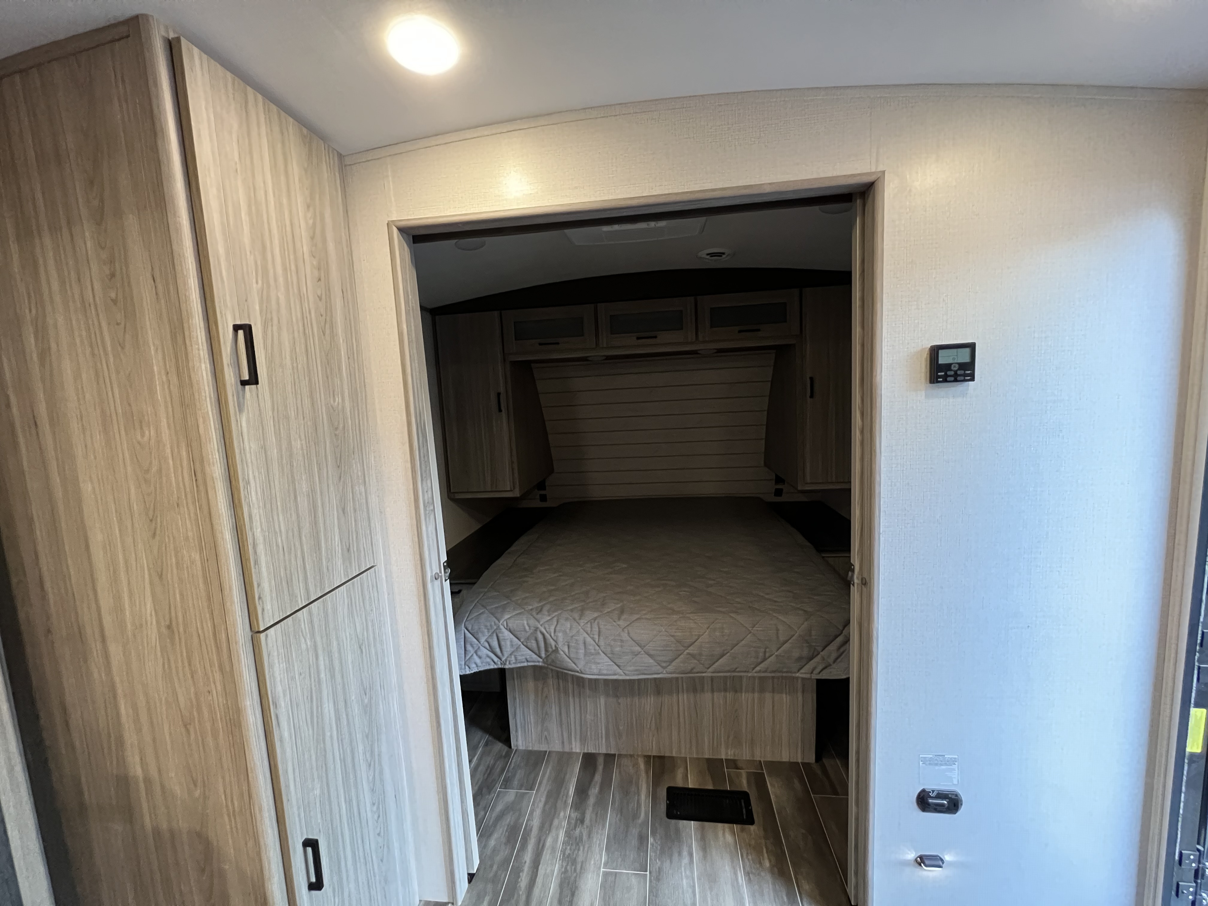 RV rental bedroom interior with a comfortable bed, light wood cabinets, and a wall-mounted control panel.. Keystone Passport 2022