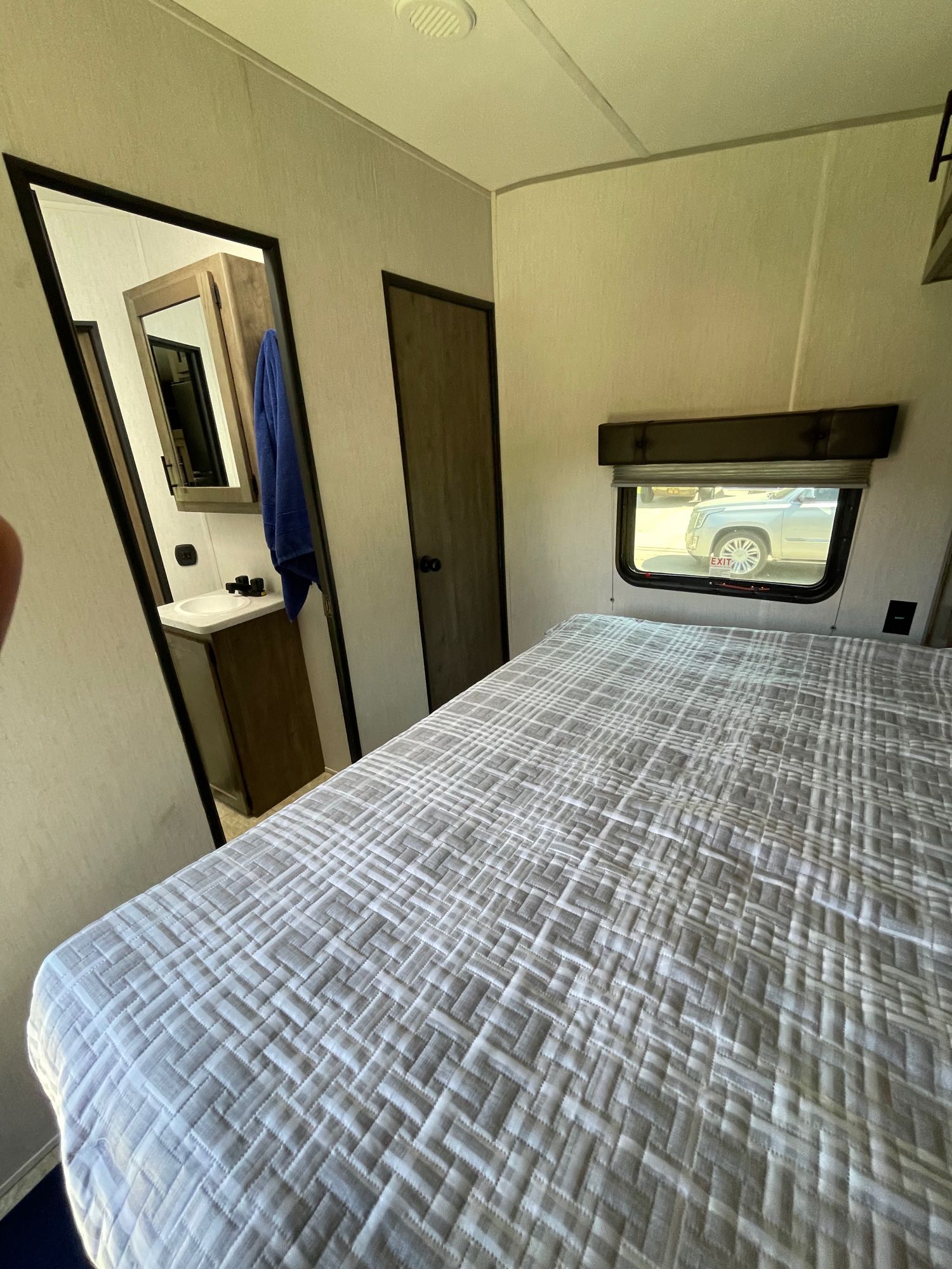 This RV rental bedroom features a patterned comforter on the bed, a window view, and access to a compact bathroom with a sink.. Forest River Vengeance 2022