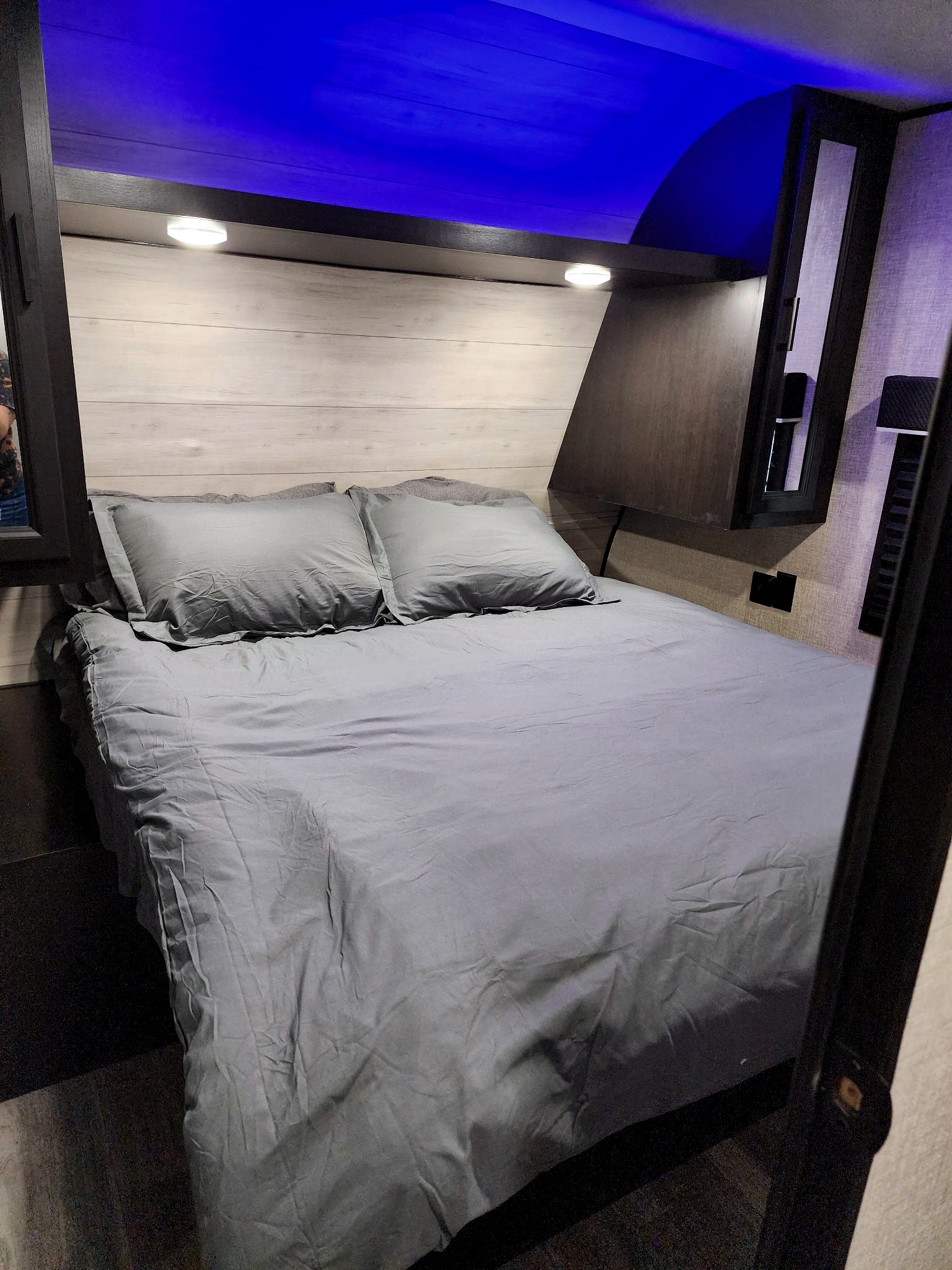 Inside an RV rental: A compact bedroom with grey-dressed bed, wooden headboard, and striking blue ceiling lights.. Jayco Jay Flight 2022