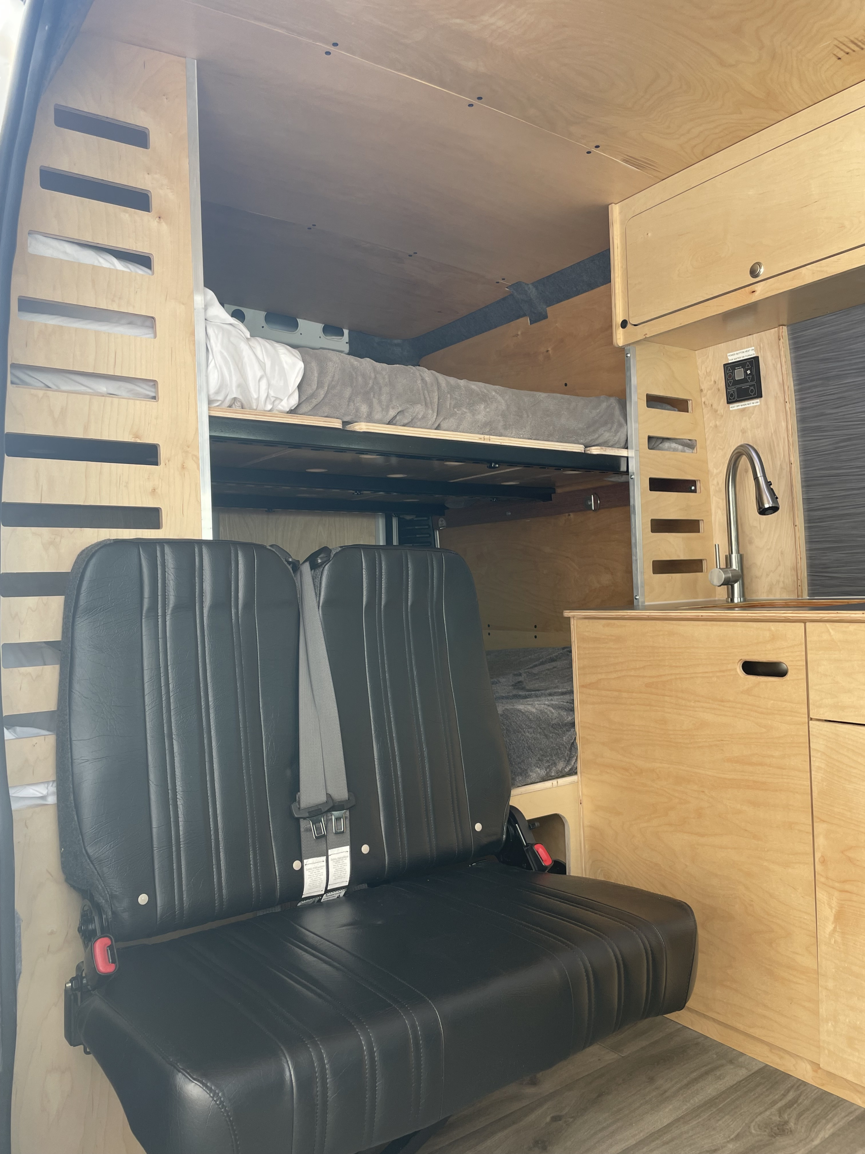 RV rental van interior: stacked wooden bunk beds, black passenger seating, and a functional kitchen sink area.. RAM ProMaster 2022