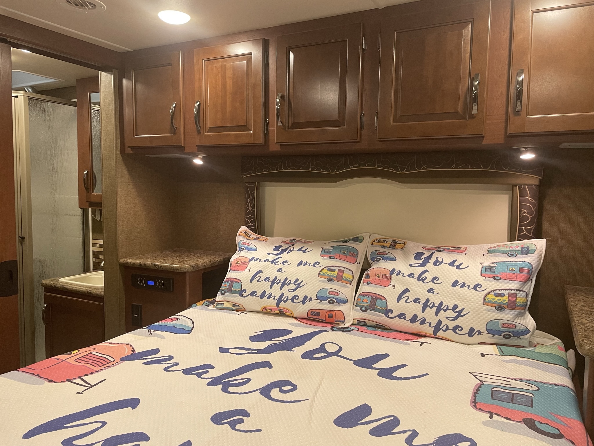 Cozy RV rental bedroom with camper-themed bedding, overhead cabinets, and an adjacent bathroom for comfortable travels.. Thor Chateau 2016