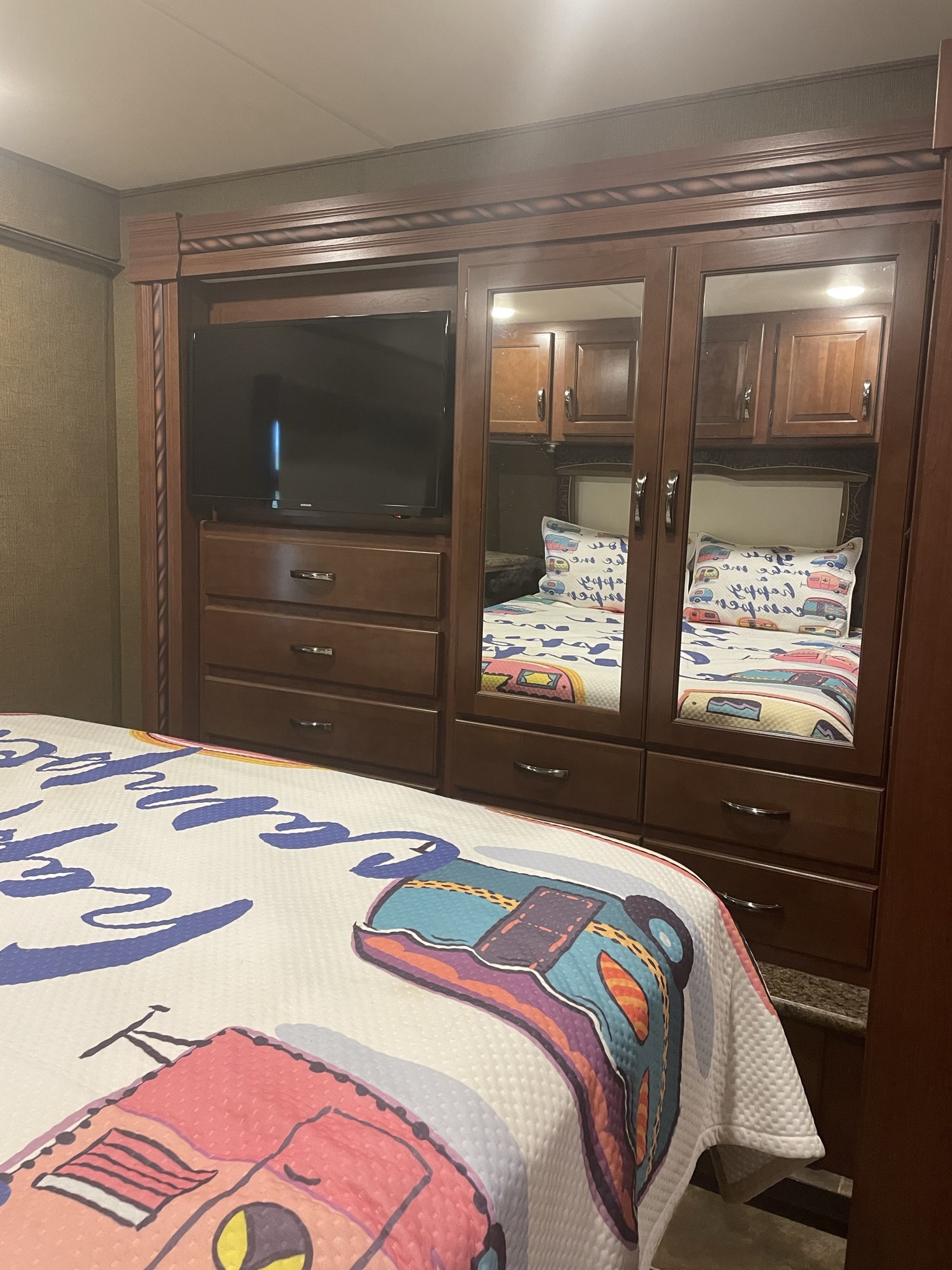 Cozy RV rental bedroom with a colorful camper quilt, built-in TV, drawers, and a mirrored wardrobe reflecting the bed.. Thor Chateau 2016
