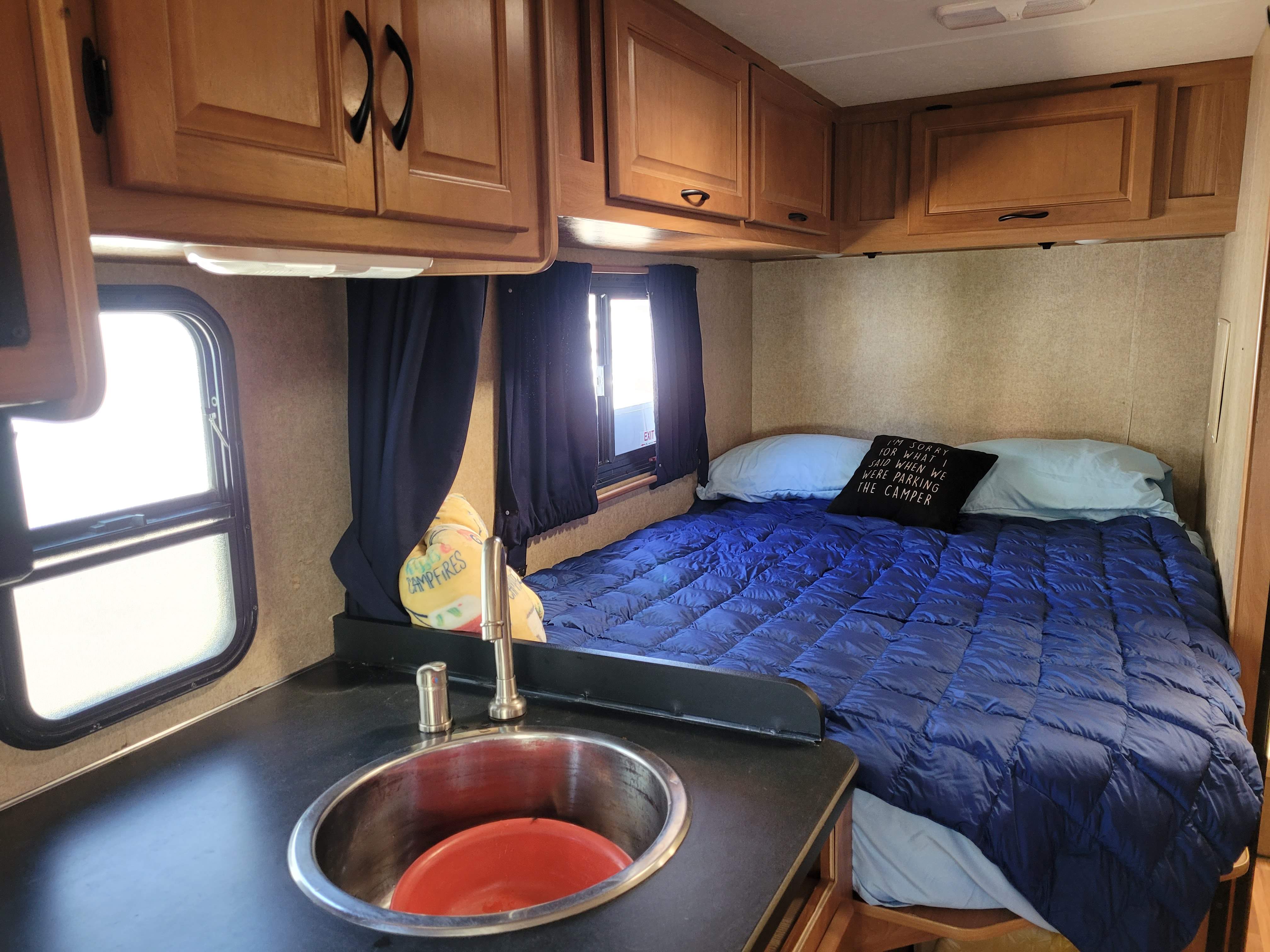 Cozy RV rental interior featuring a bed with blue bedding, ample wood cabinets, and a compact sink. Ready for your travels!. Thor Majestic 2017