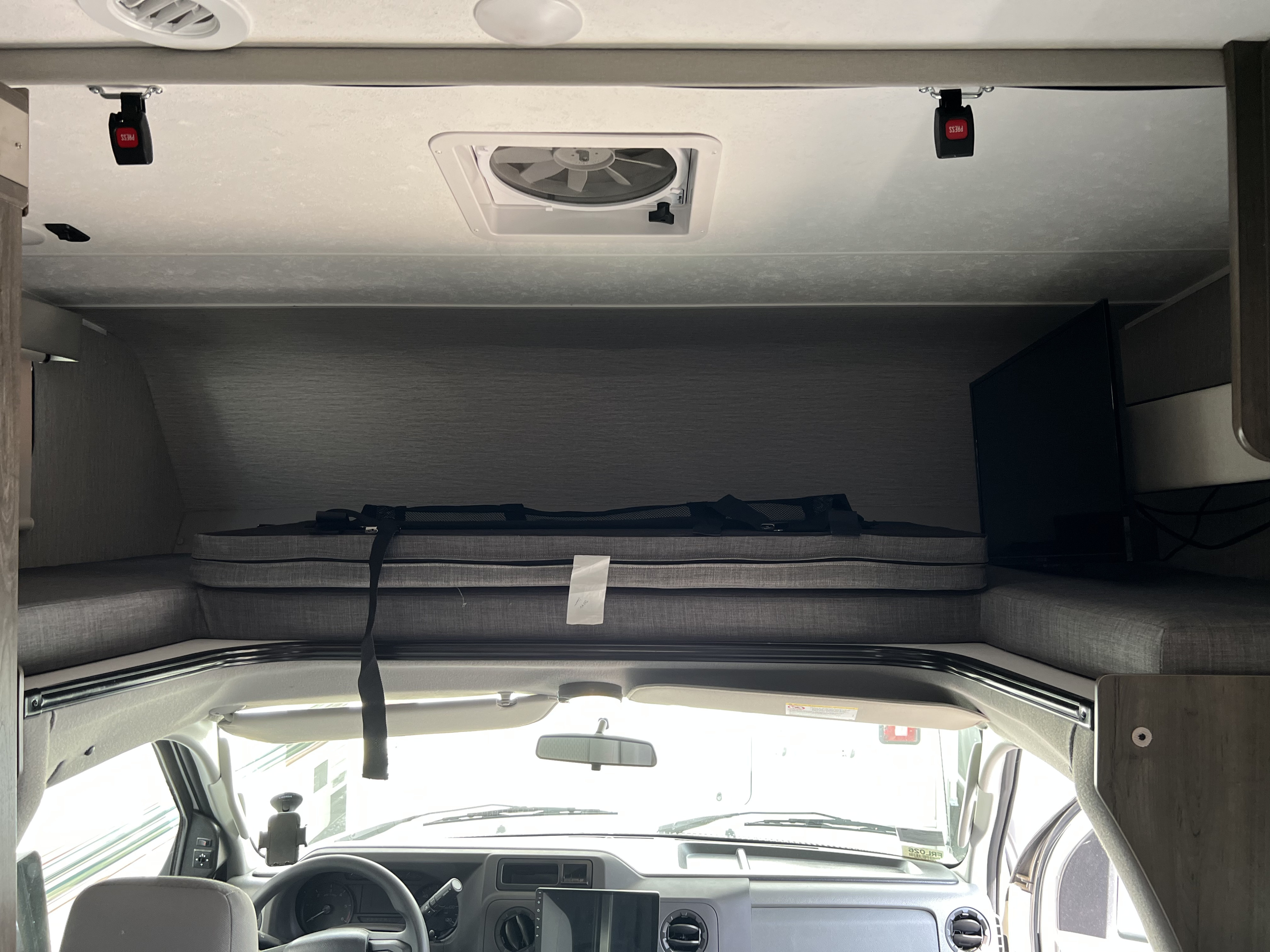 Inside an RV rental: View from the cab to the overhead sleeping bunk with folded mattresses, a fan, and TV.. Forest River Coachmen Leprechaun Premier 2022