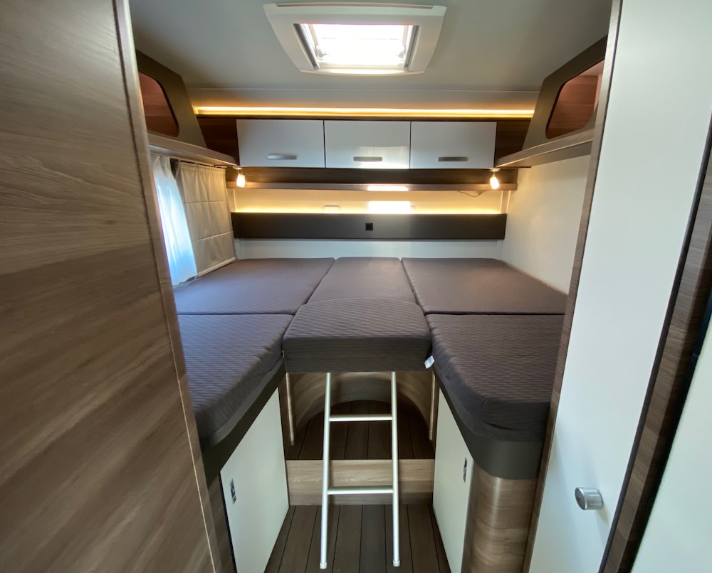 RV rental's bunk bed sleeping area, seen from doorway. Multi-level beds, ladder, overhead storage & lighting in this modern camper.. Knaus Live Wave 700 MEG 2022