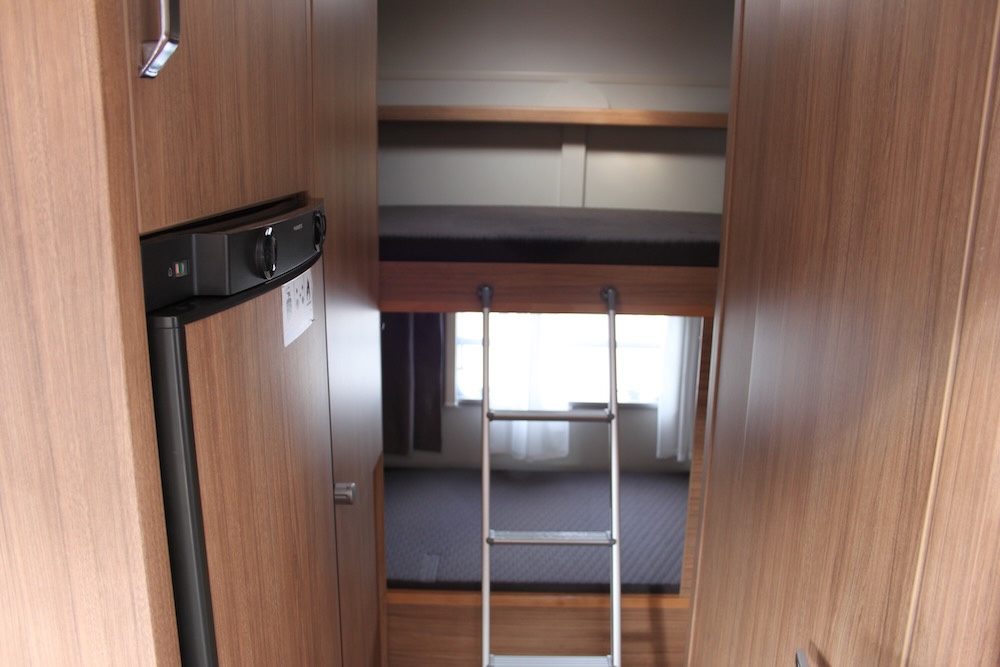 This RV rental shows a compact interior with a built-in fridge on the left and bunk beds, accessible by a ladder, at the end.. Weinsberg 600 DKG 2022